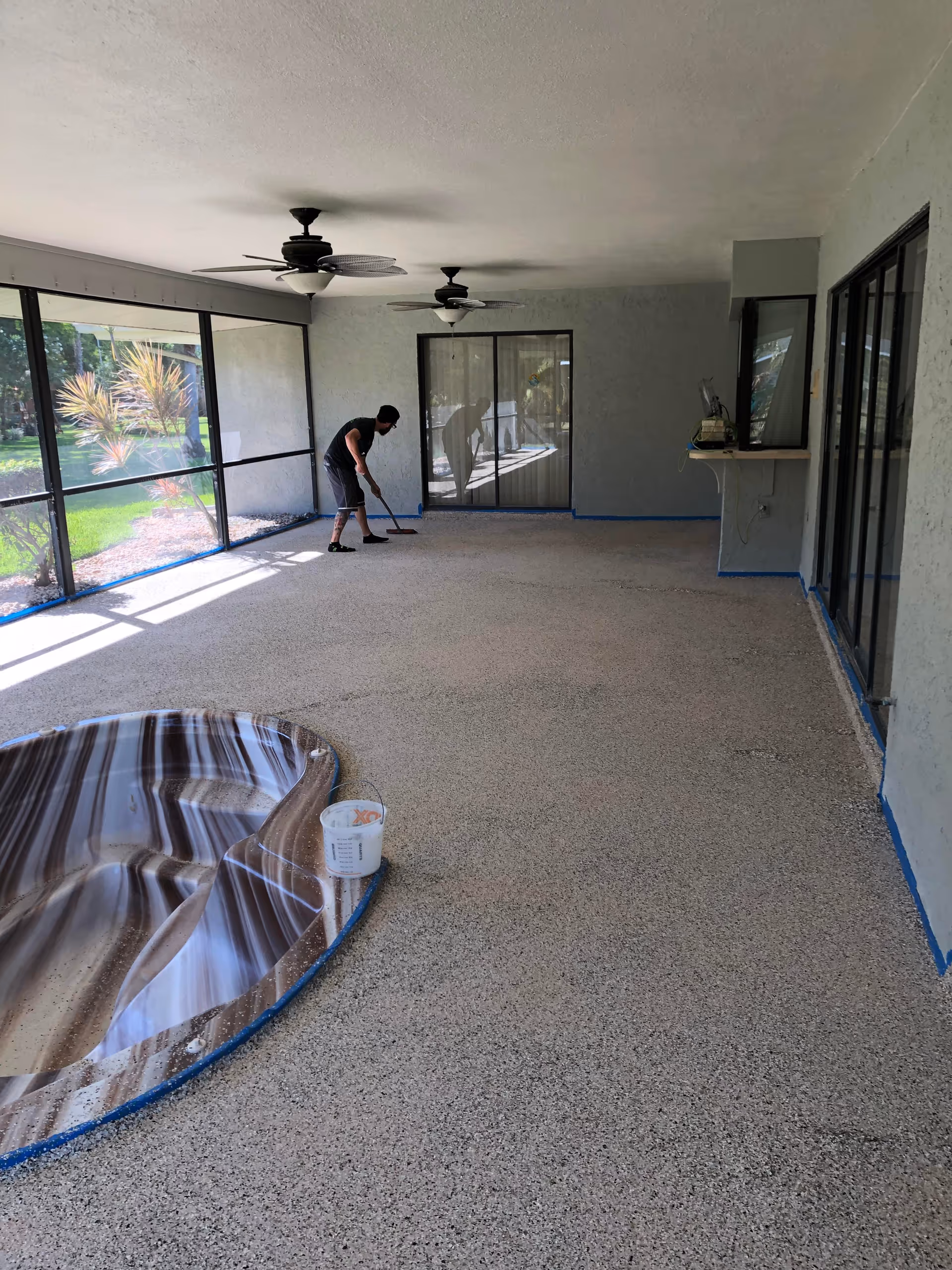 Maintenance worker sweeps a glass-walled, covered patio area inside a senior living facility.