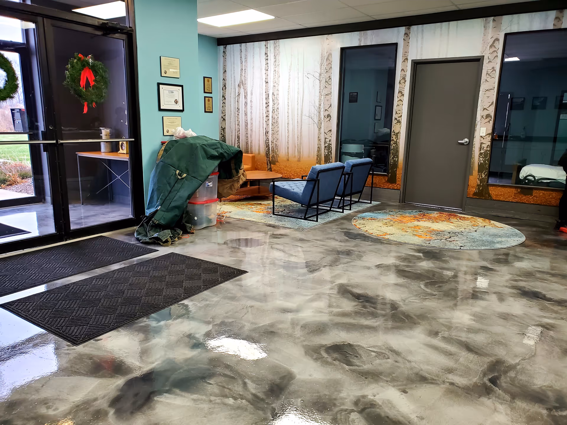 Indoor lobby area with teal walls, seating, wall mural, and a wreath on the entrance door.