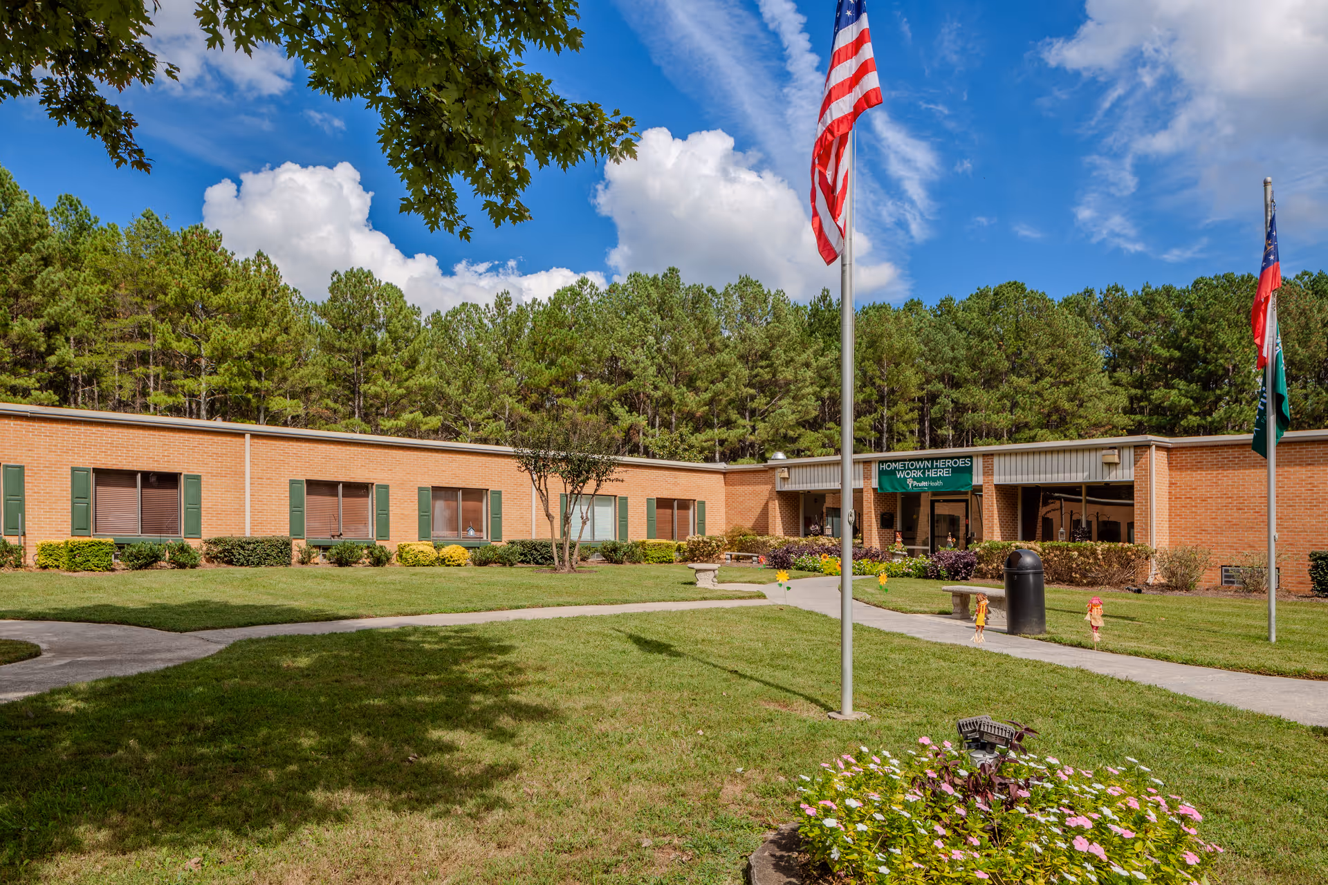 Front view of Pruitthealth Lafayette facility with flags, green lawn, and bright blue sky.
