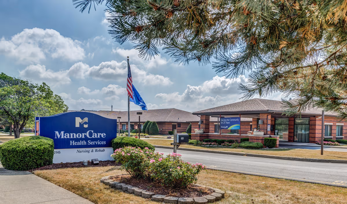 Exterior view of ManorCare Health Services facility with front entrance, sign, and manicured landscaping.