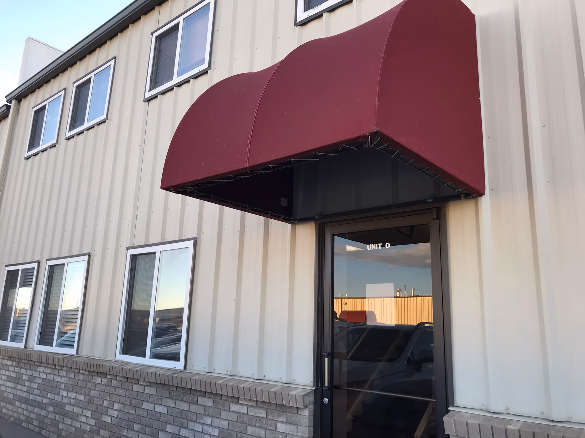Exterior of a facility entrance with a maroon curved awning and UNIT 0 door.