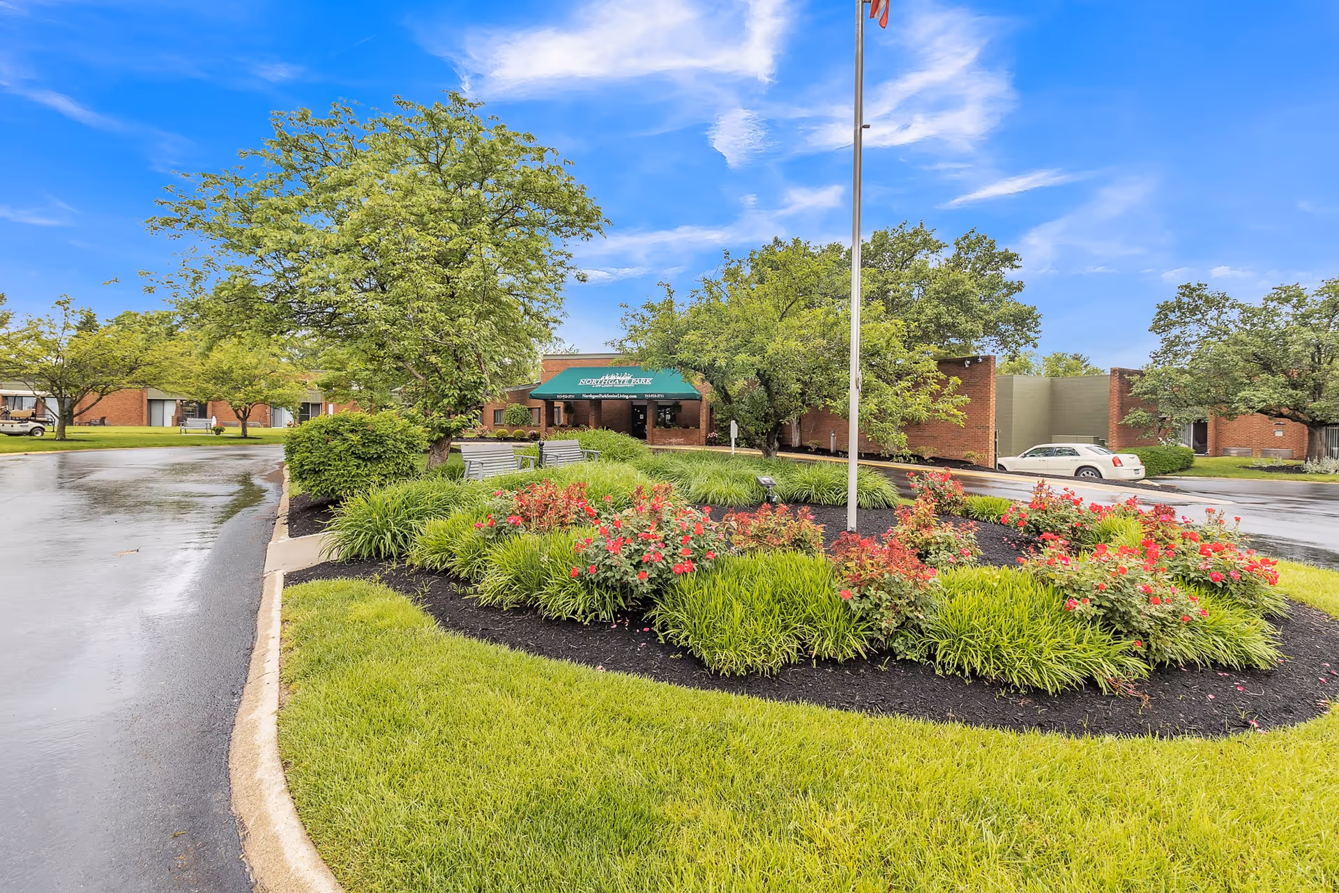 Landscaped circular flower bed and flagpole in front of a brick building's covered entrance with a green awning.