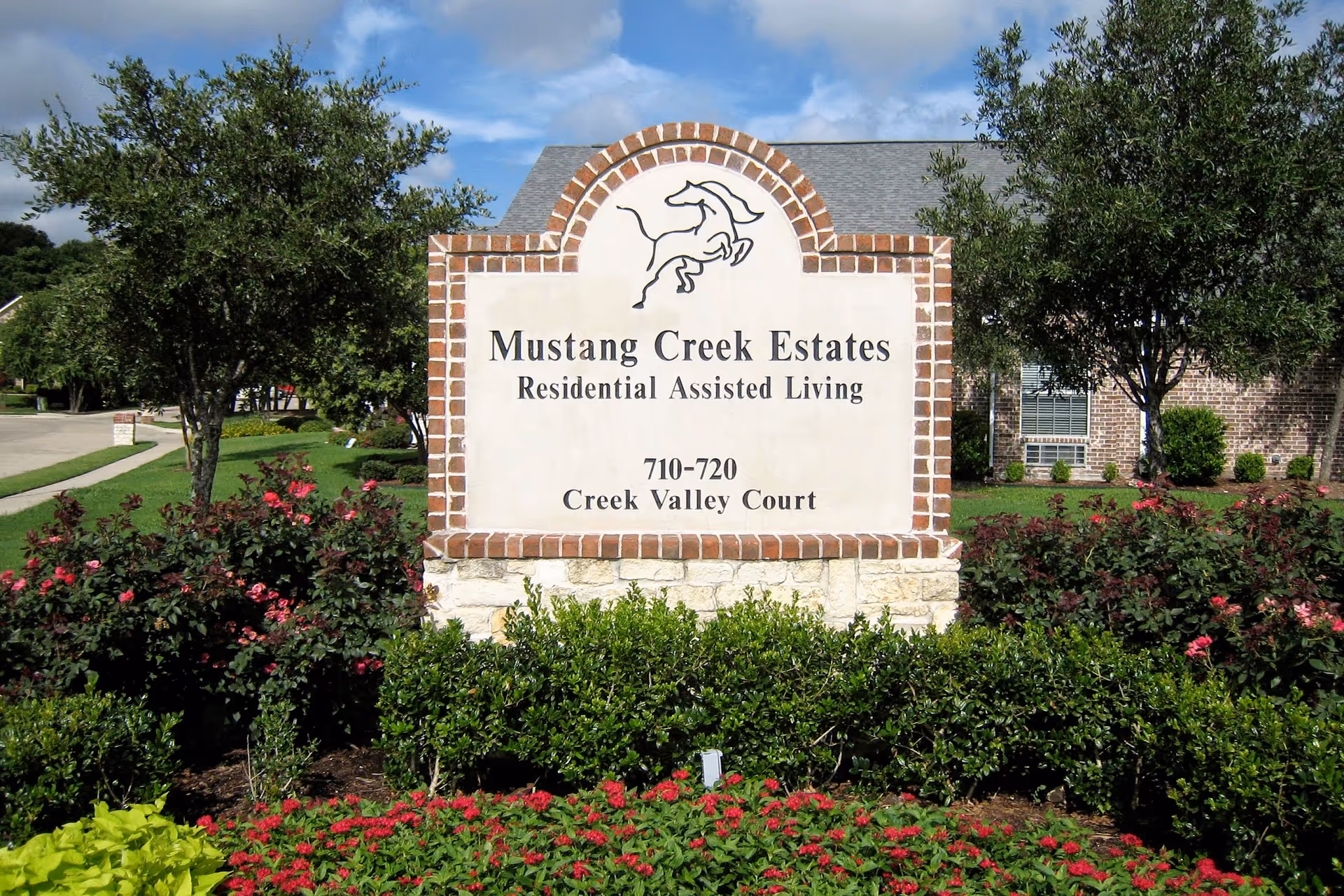 Front exterior view of Mustang Creek Estates Allen sign surrounded by greenery and flowers.