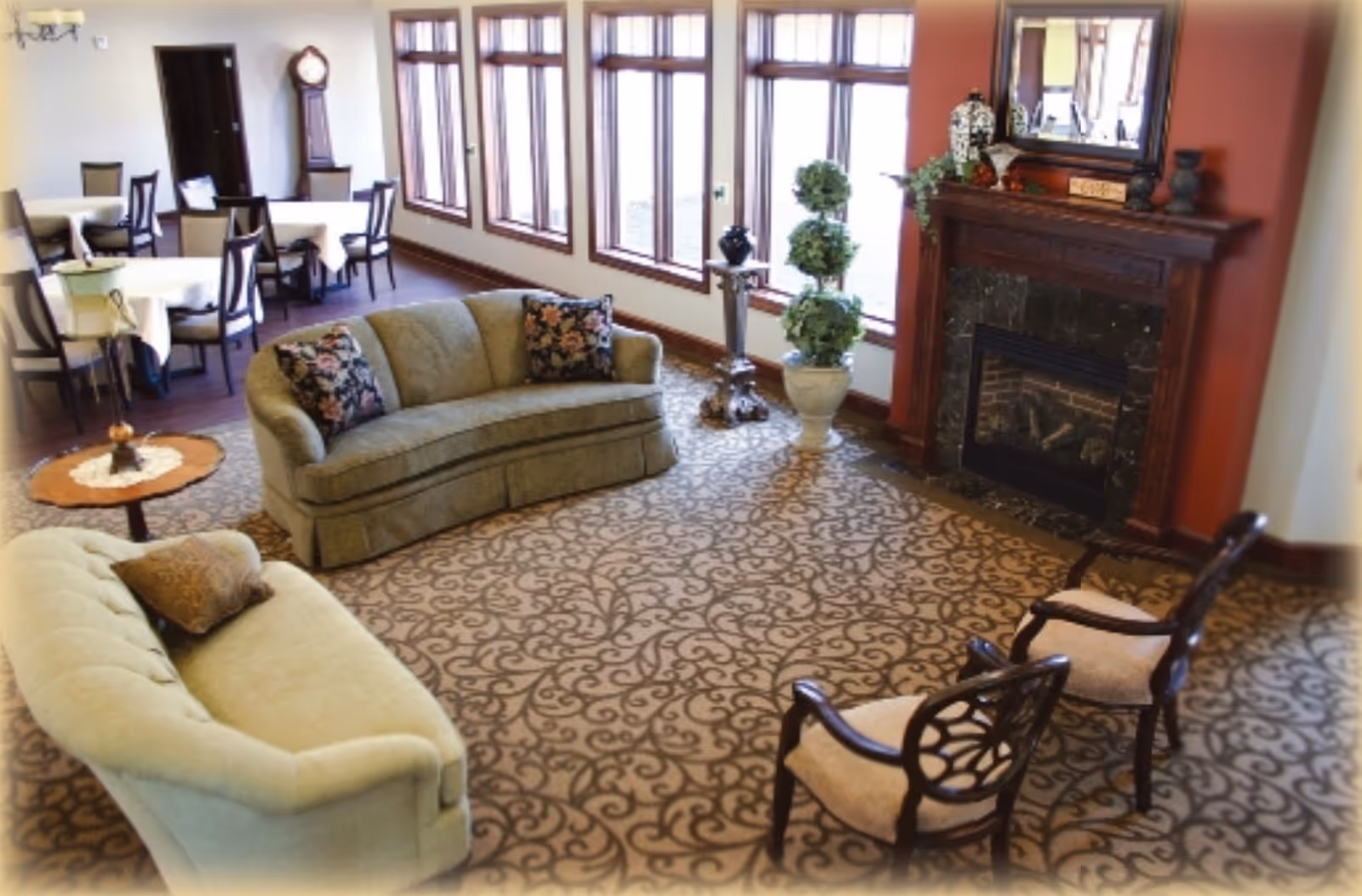 Cozy senior living lounge featuring sofas, chairs, a fireplace, and potted plants.