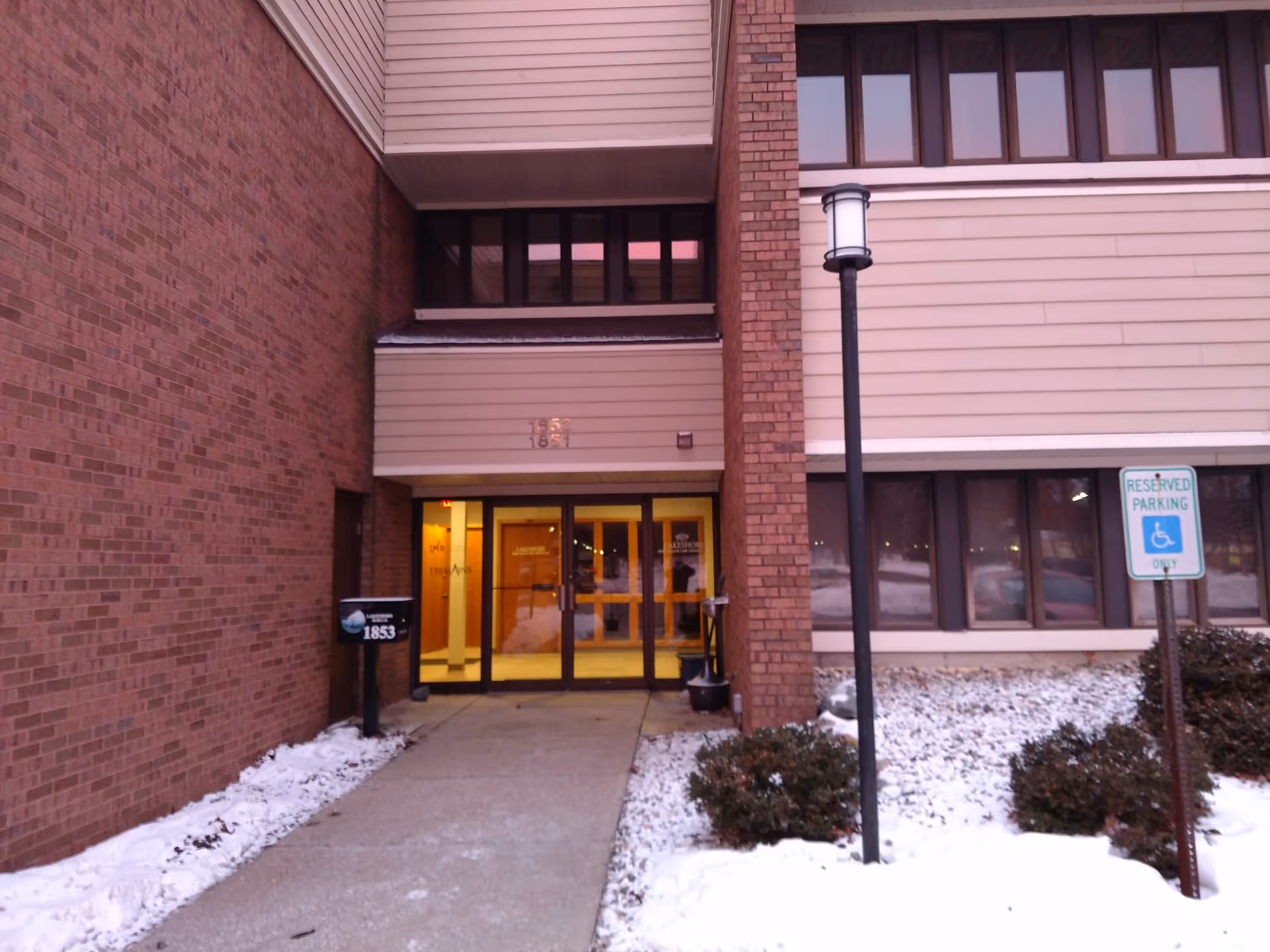 Brick exterior of a building entrance with glass doors and a snow-covered walkway.