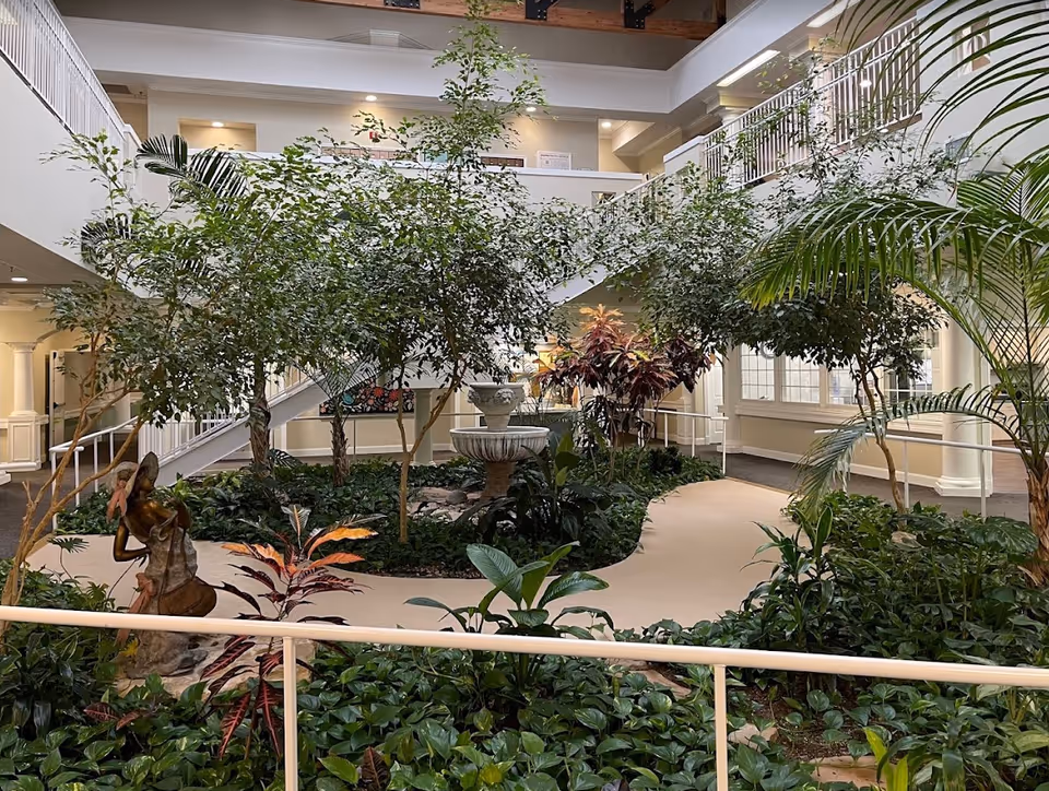 Indoor atrium with lush plants, a central fountain and sculpture, walkways and surrounding balconies inside the facility.