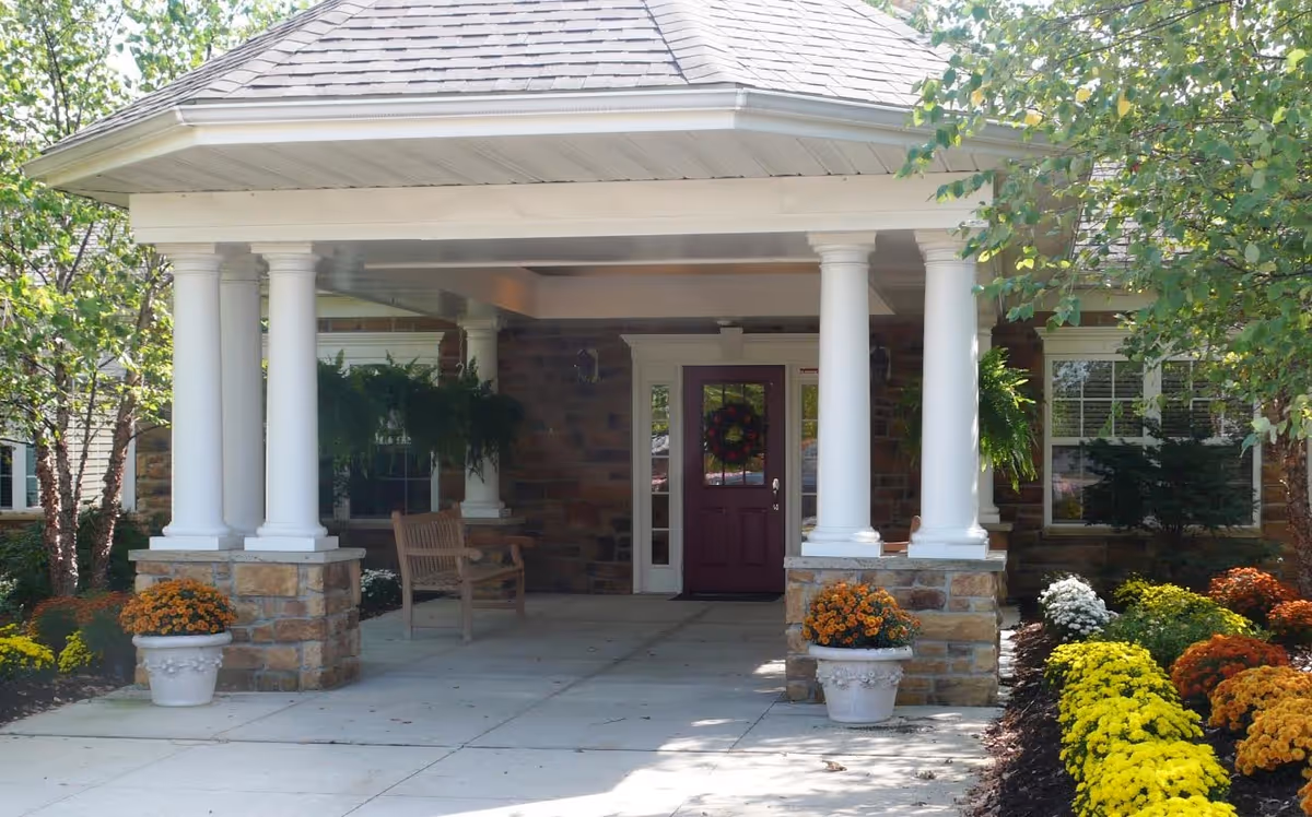Covered front porch with white columns, a maroon door, and potted flowers with greenery.