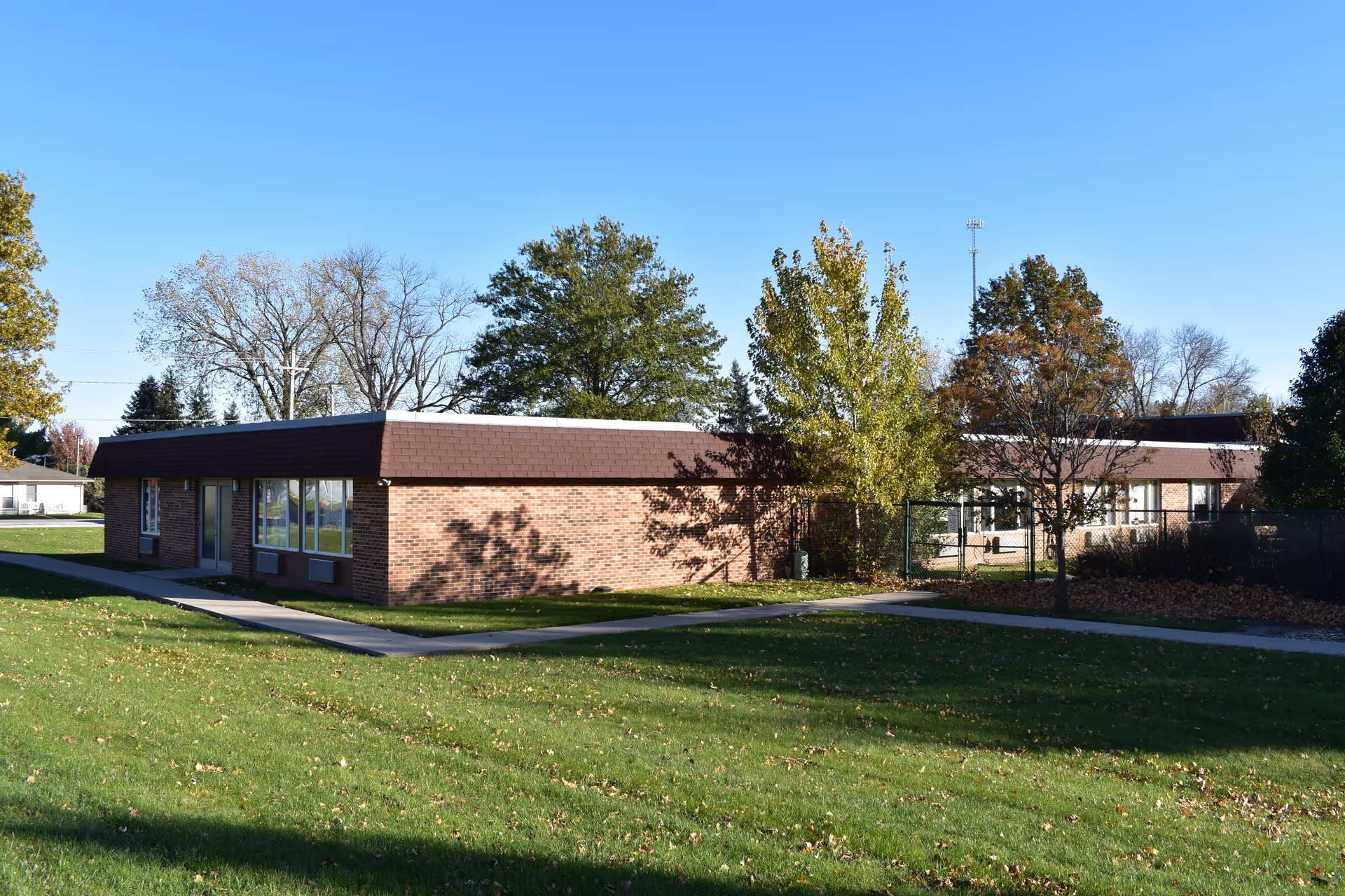 Single story brick senior living facility exterior with windows, trees, and a grassy lawn.