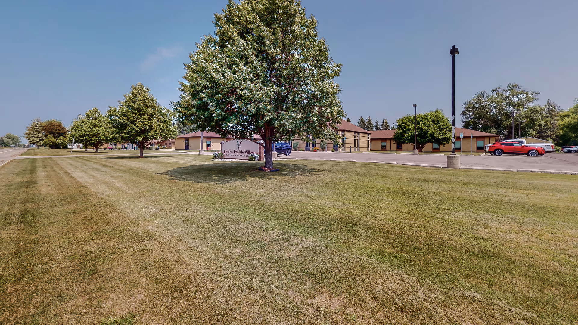 Exterior view of Hatton Prairie Village with a green lawn and parked cars.