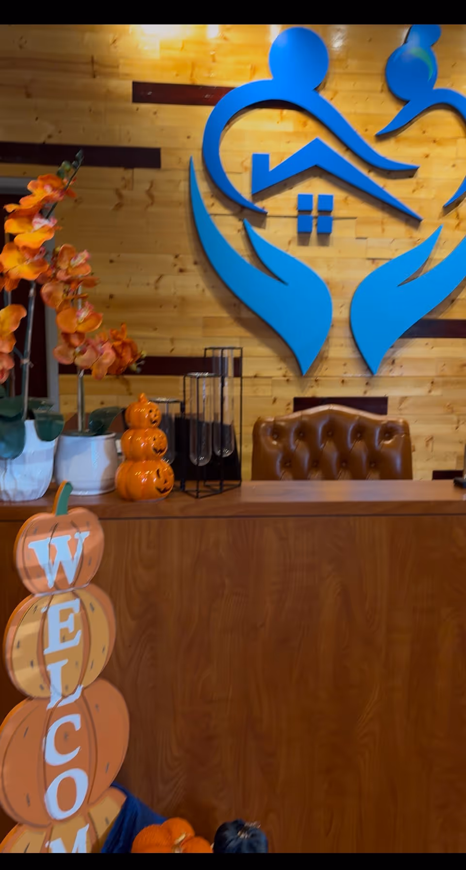Indoor reception area with a wooden desk, blue logo, and fall decorations.