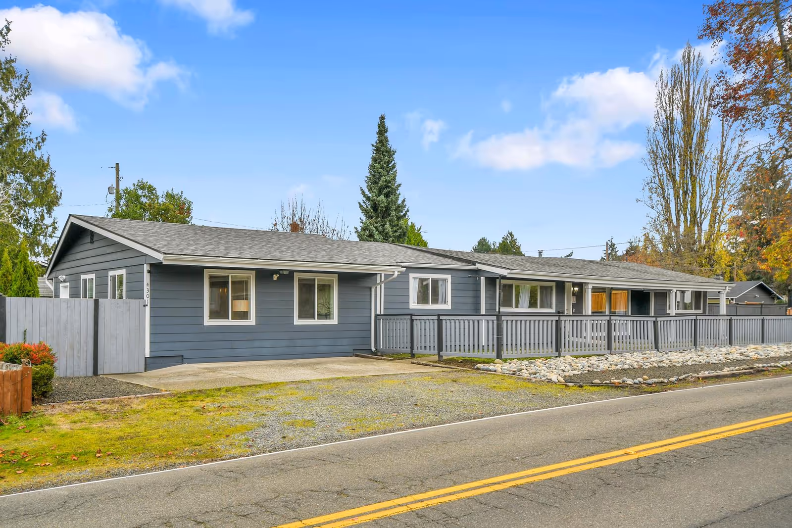 Single-story blue adult family home with long front porch along a quiet street.