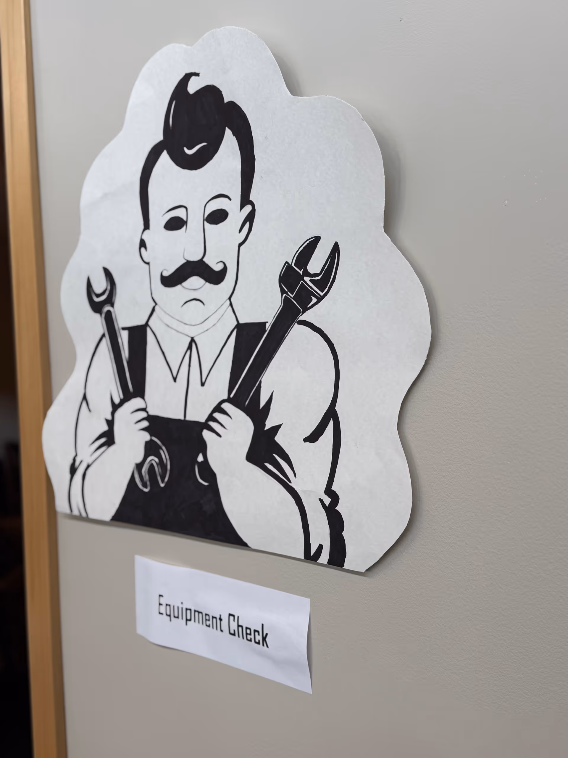 Wall-mounted cartoon handyman holding wrenches beside an Equipment Check sign.