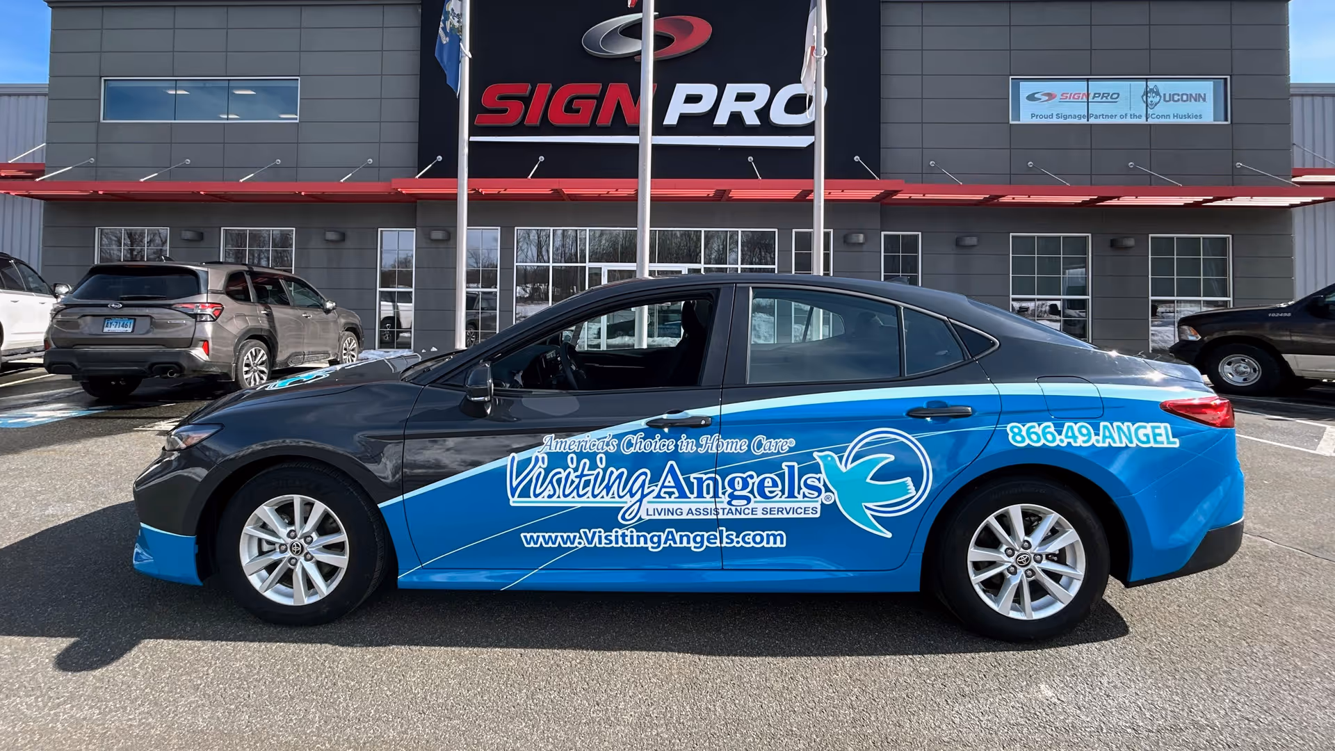 Blue Visiting Angels promotional car parked in front of a commercial building.