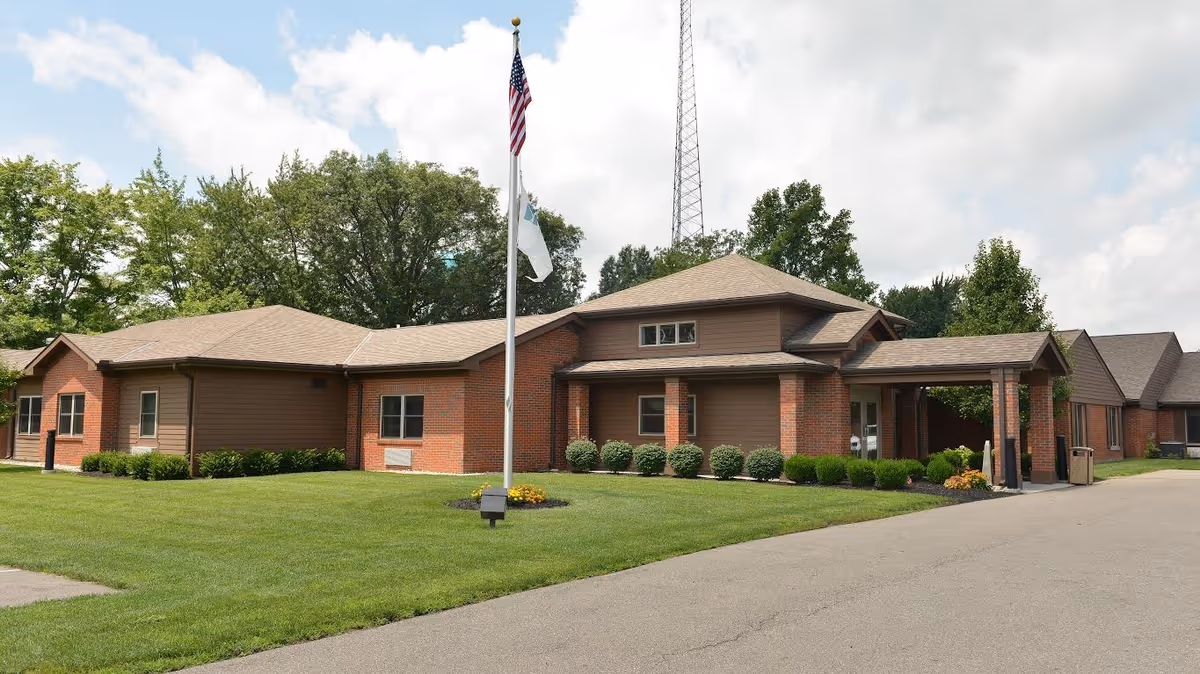 Single-story brick building with a covered entrance, flagpole, and landscaped lawn.