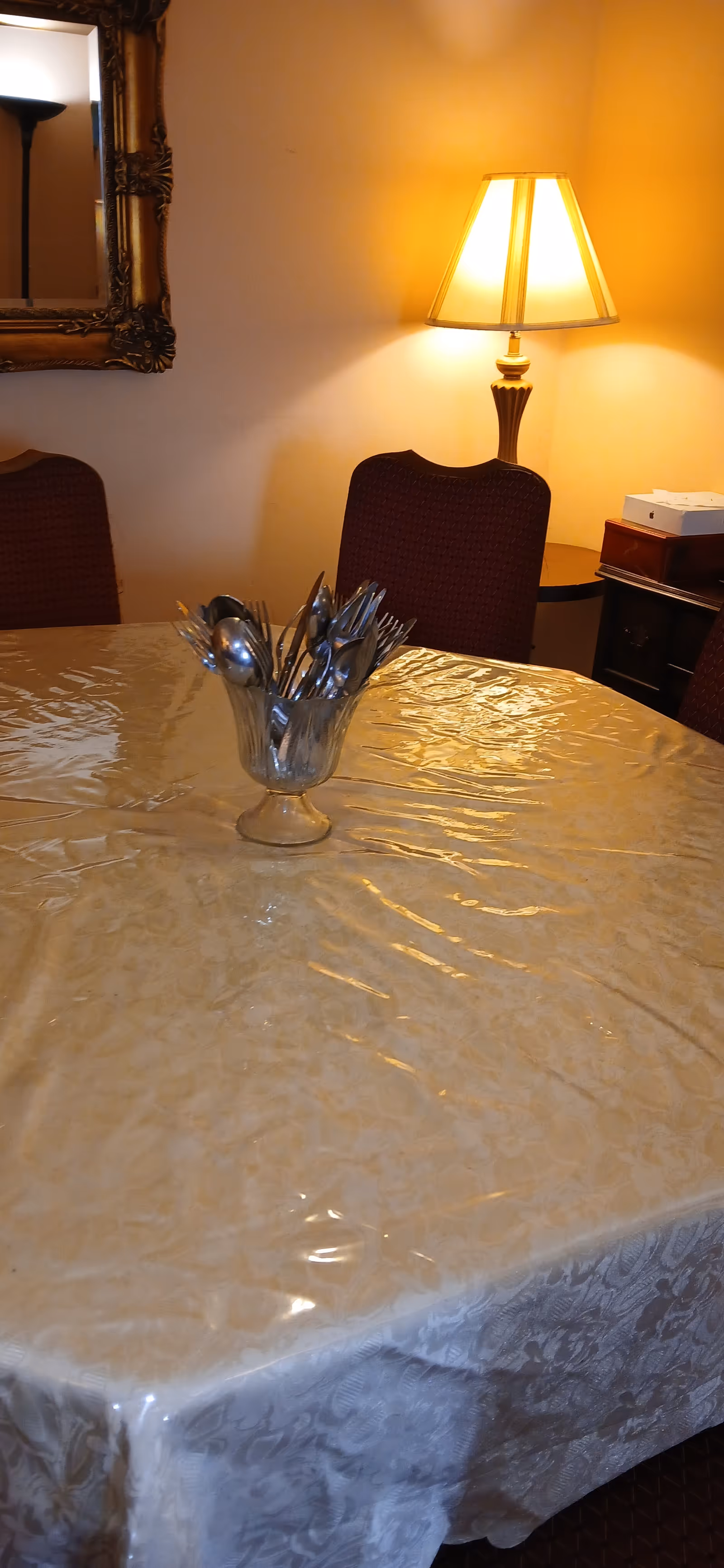 A dining table covered with plastic, surrounded by red upholstered chairs under a warm lamp.