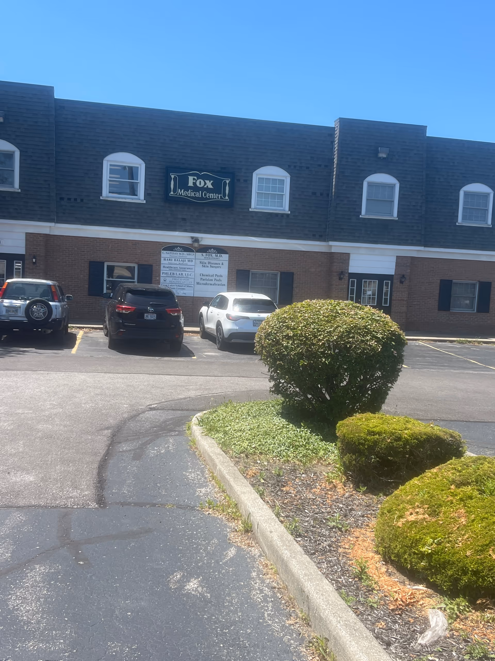 Front view of a brick medical center with parked cars and manicured shrubs.