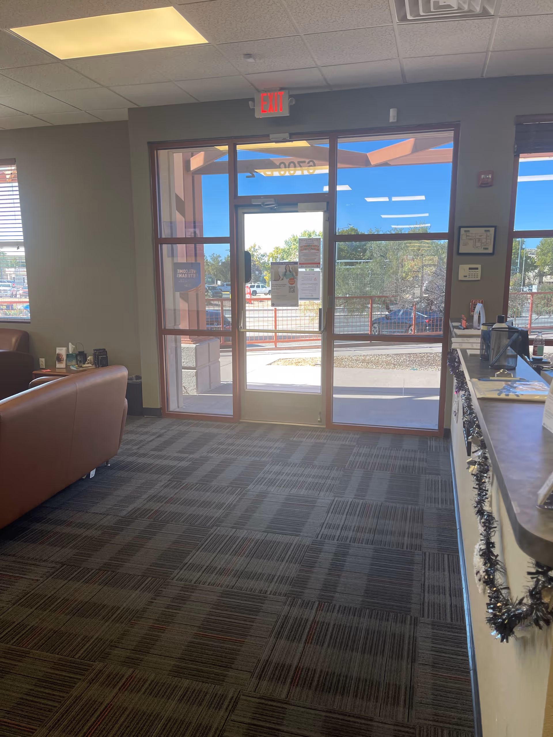 Lobby area with glass doors, exit sign, brown leather seating, and a decorated counter.