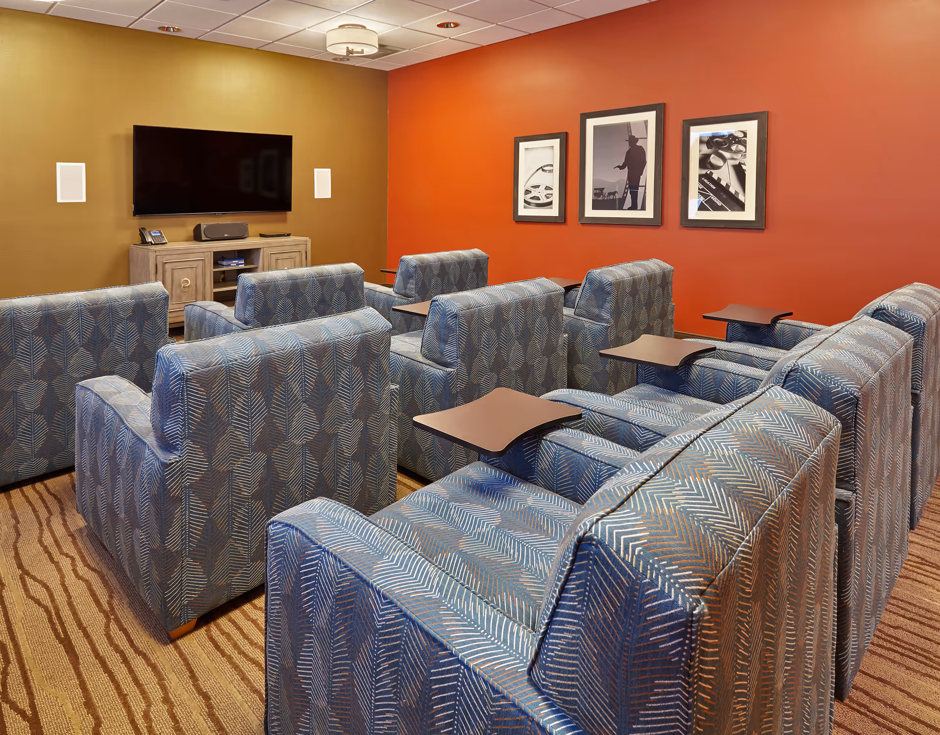 Senior living facility lounge with blue patterned chairs and a wall-mounted TV.