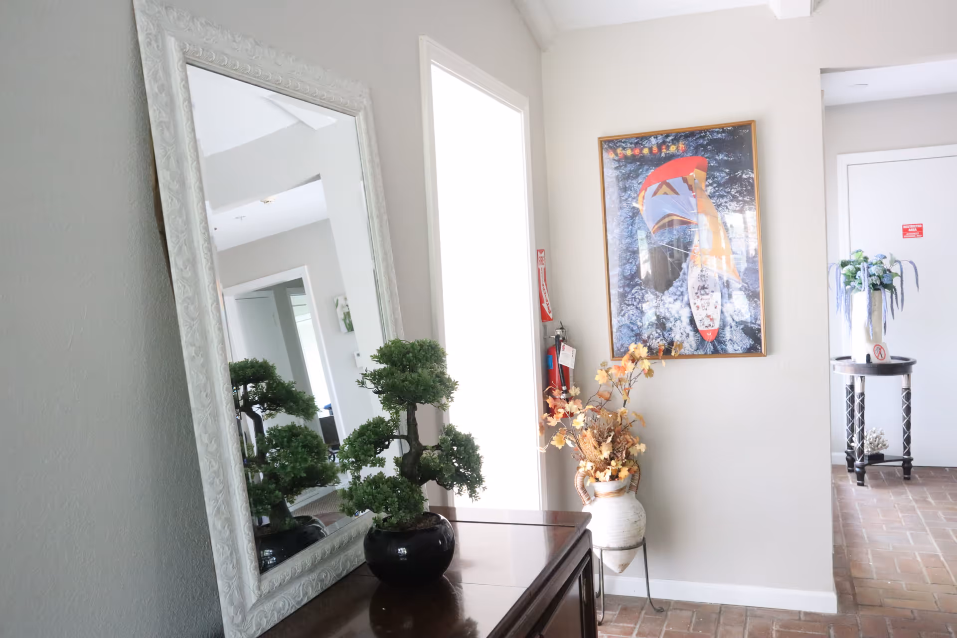 Interior entryway with a large framed mirror, a potted bonsai on a console table, framed artwork, and decorative vases.
