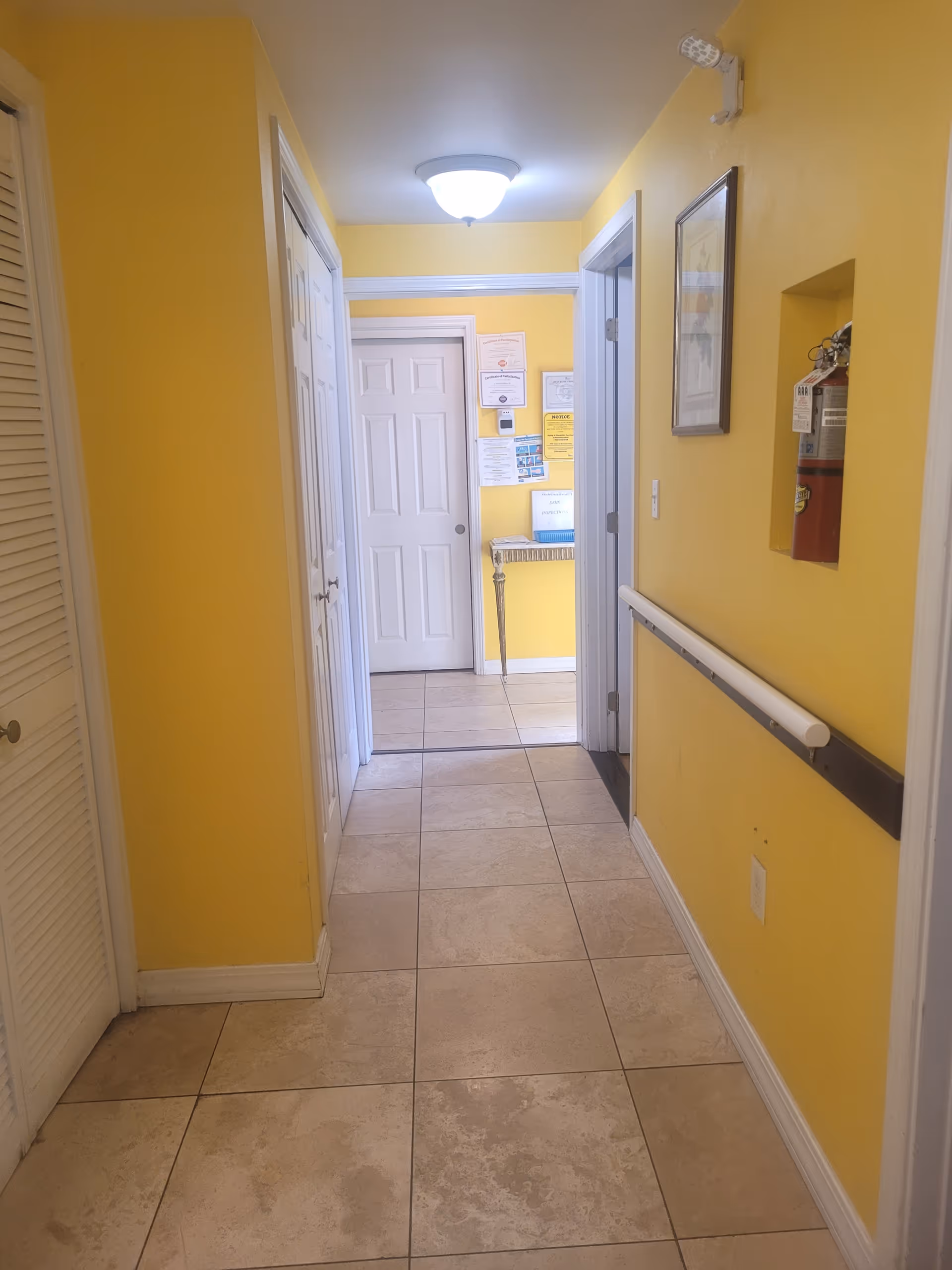 Yellow-walled hallway in a senior living facility with tiled floor and a handrail.