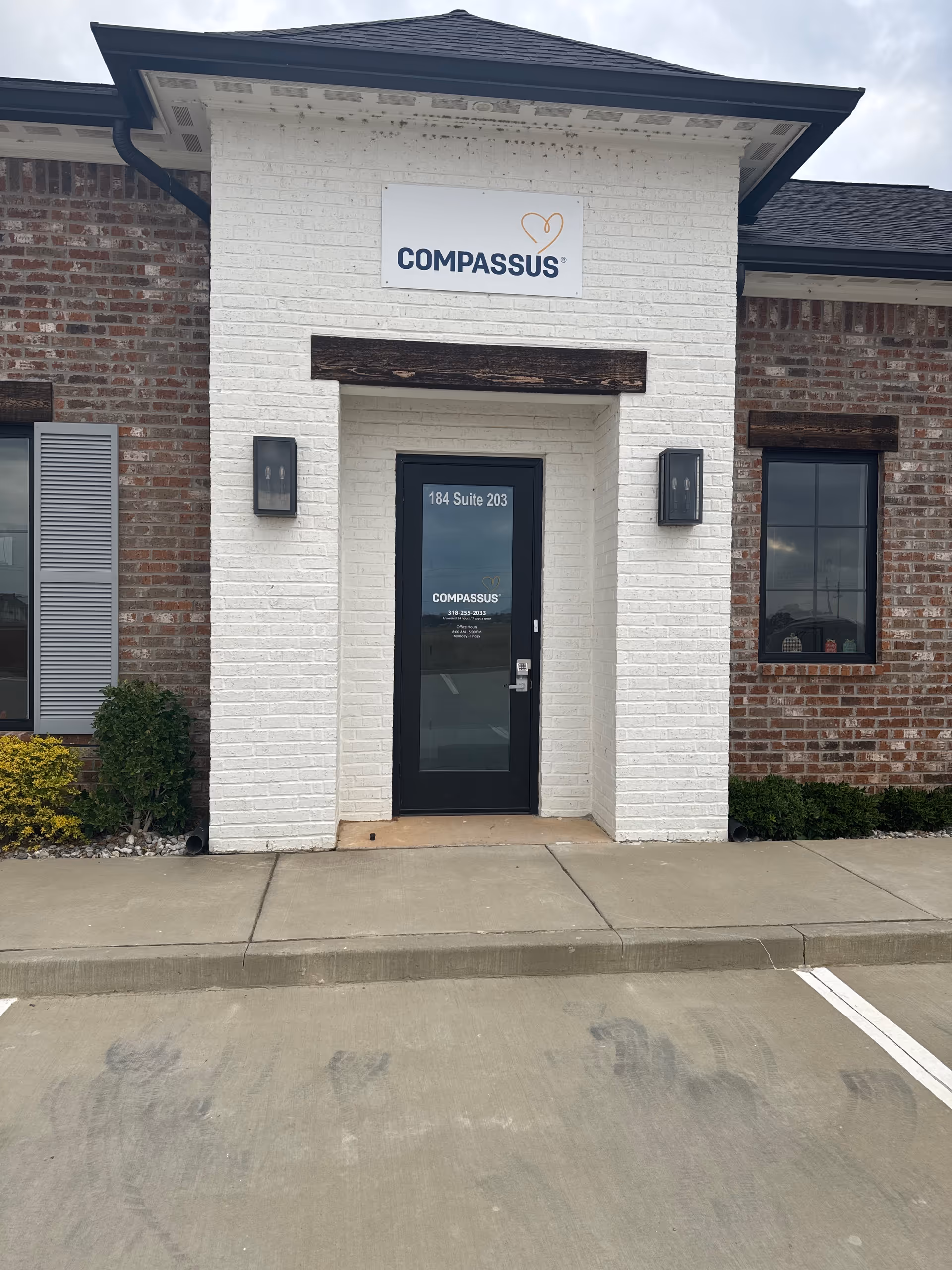 Front entrance of a Compassus senior living facility with glass door and sign.