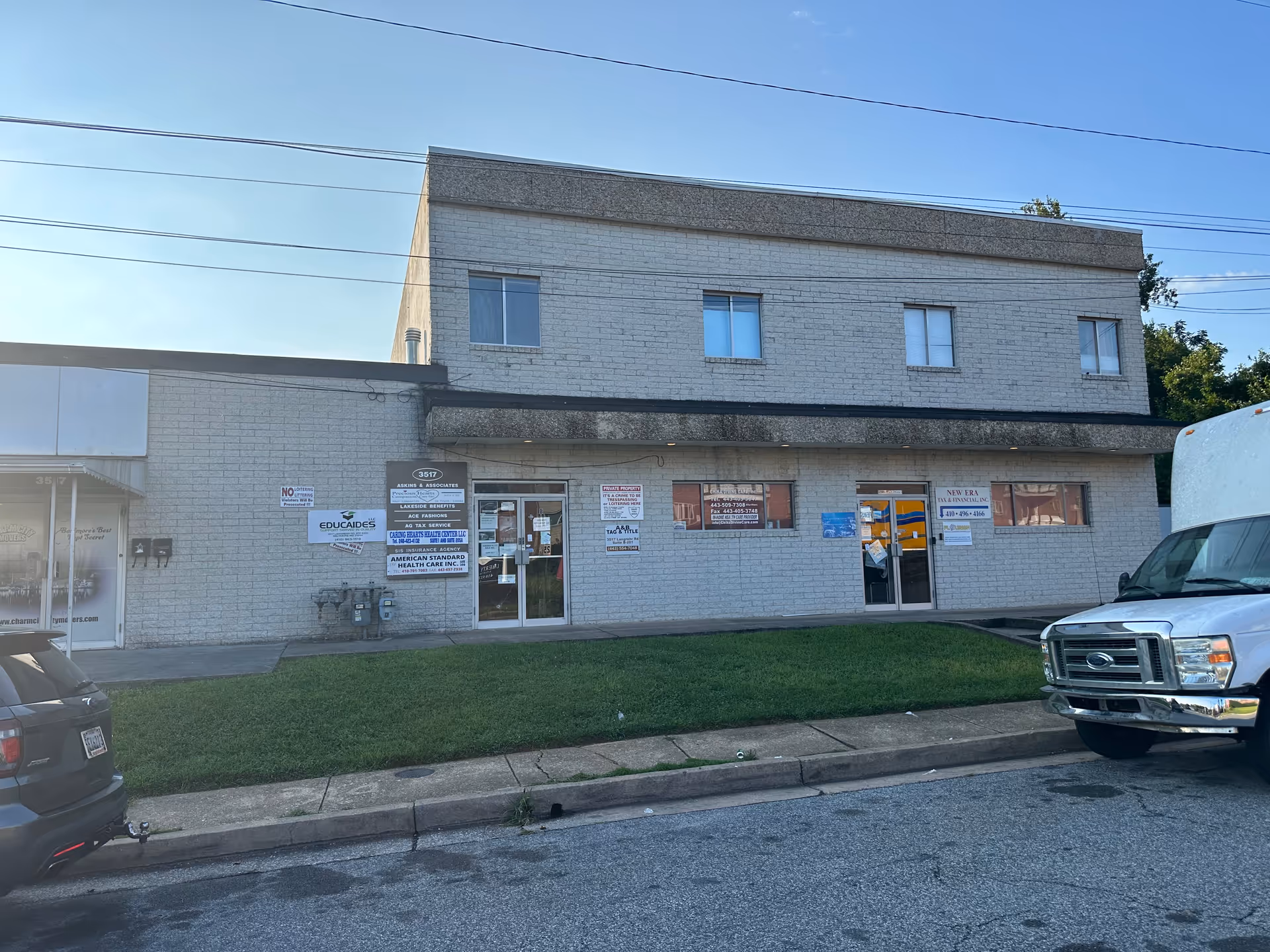 Two-story brick commercial building with storefronts and multiple signs on the exterior, parked vehicles nearby.