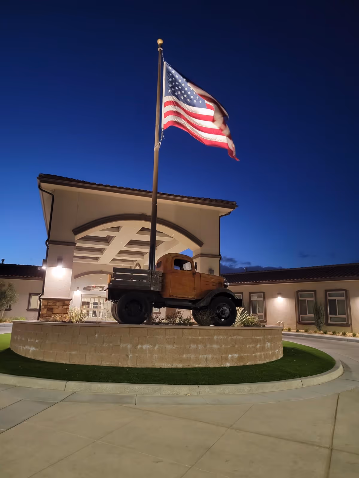 Exterior view of Desert Ridge Transitional Care Center with a vintage truck sculpture and American flag.