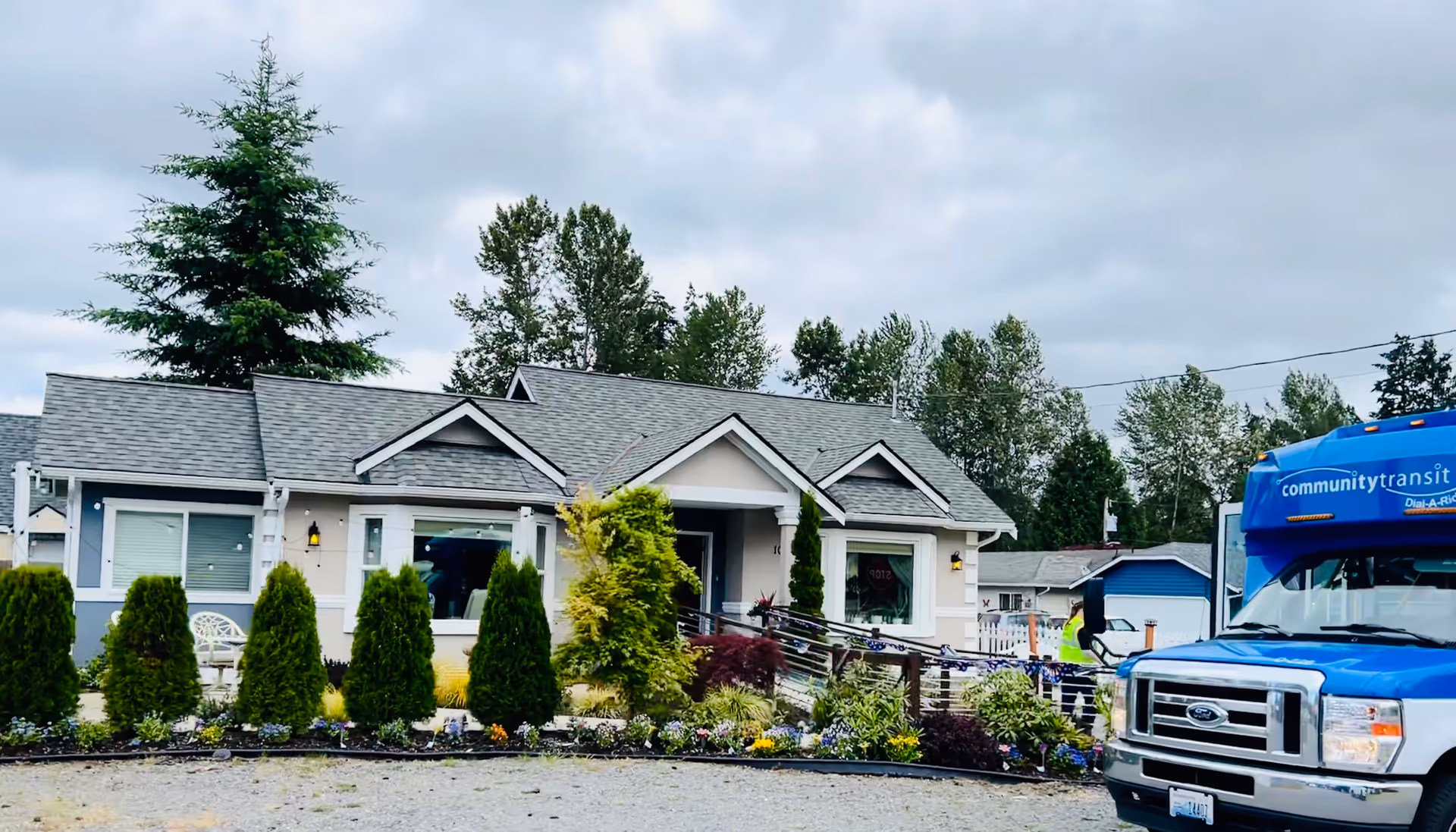 Single-story senior living facility exterior with trimmed shrubs and a blue transit bus nearby.