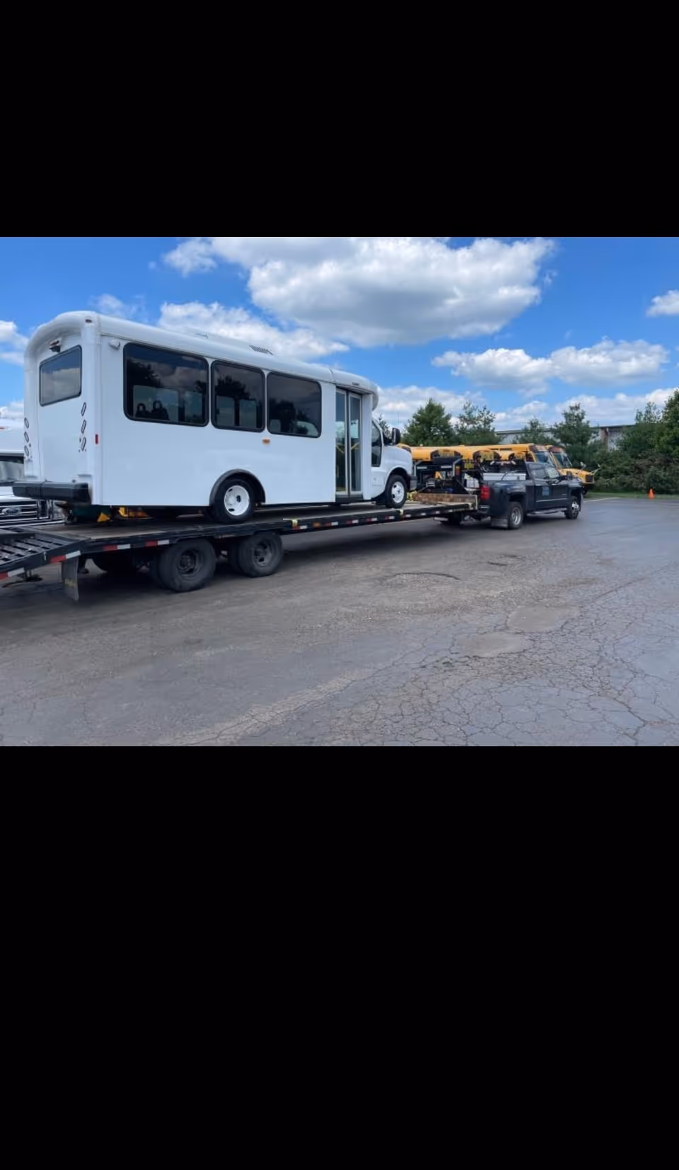 White shuttle bus loaded on a trailer in a parking lot.