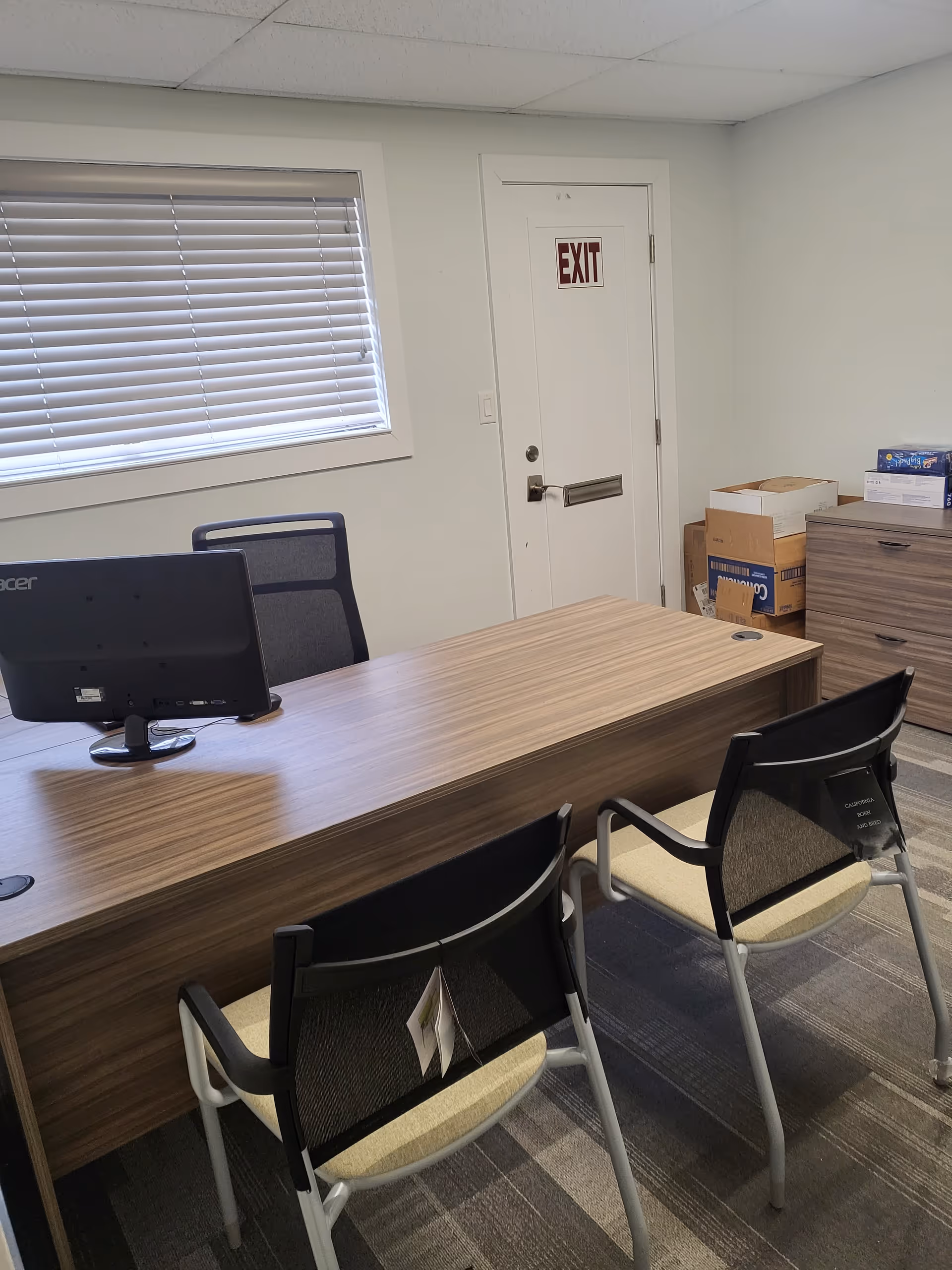 Reception desk with computer and two chairs beside an EXIT door in a small interior office.
