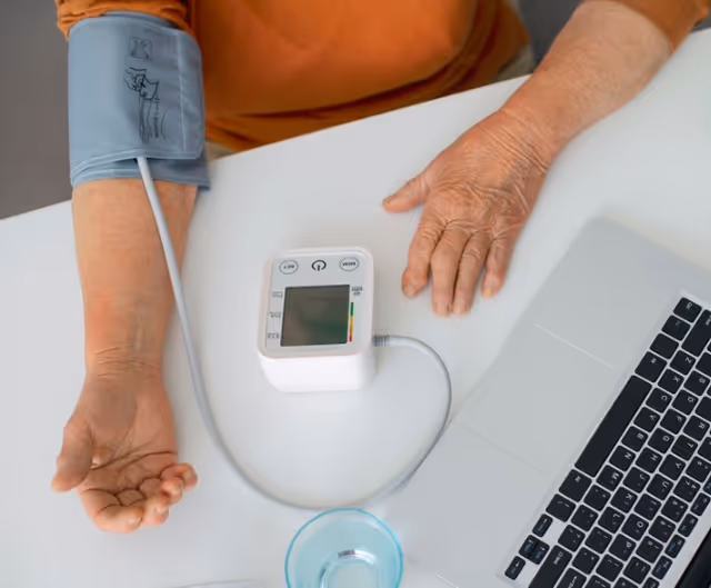 Patient's arm with blood pressure cuff and monitor beside a laptop on a table.