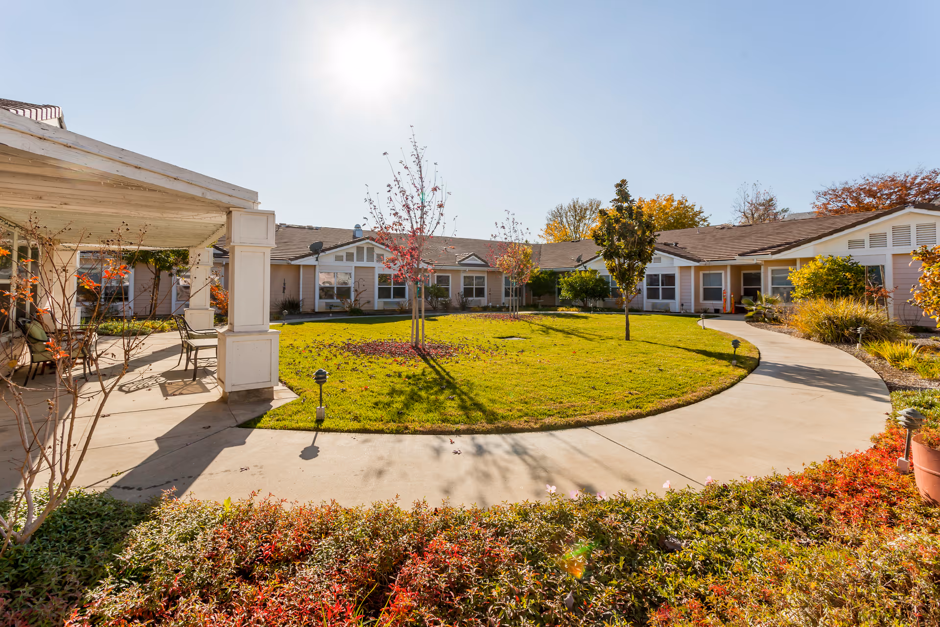 Sunny outdoor courtyard with curved walkway, lawn, and single-story Lassen House Senior Living buildings.