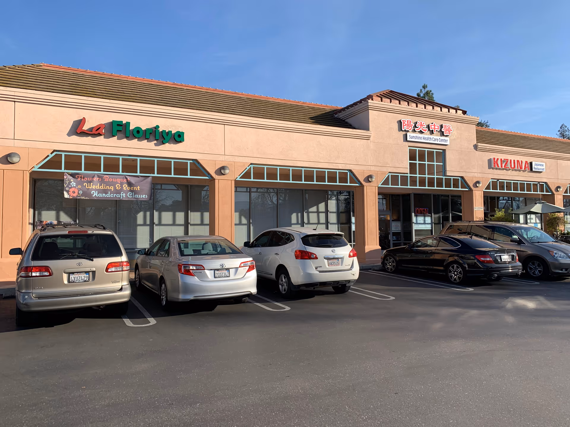 Exterior view of a strip mall with a Sunshine Health Care Center sign and parked cars.