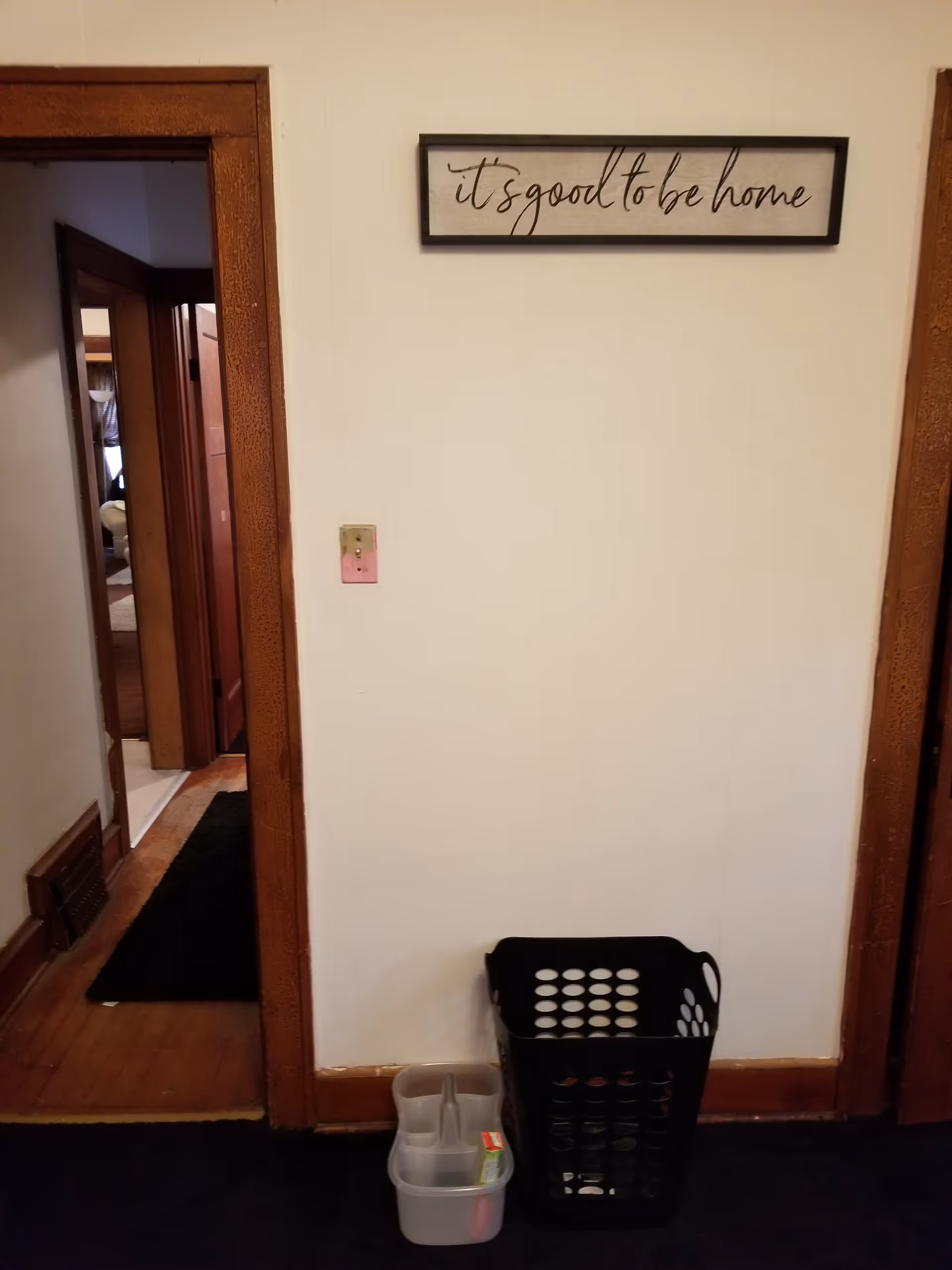 Interior hallway with a framed sign, doorway, and laundry basket.