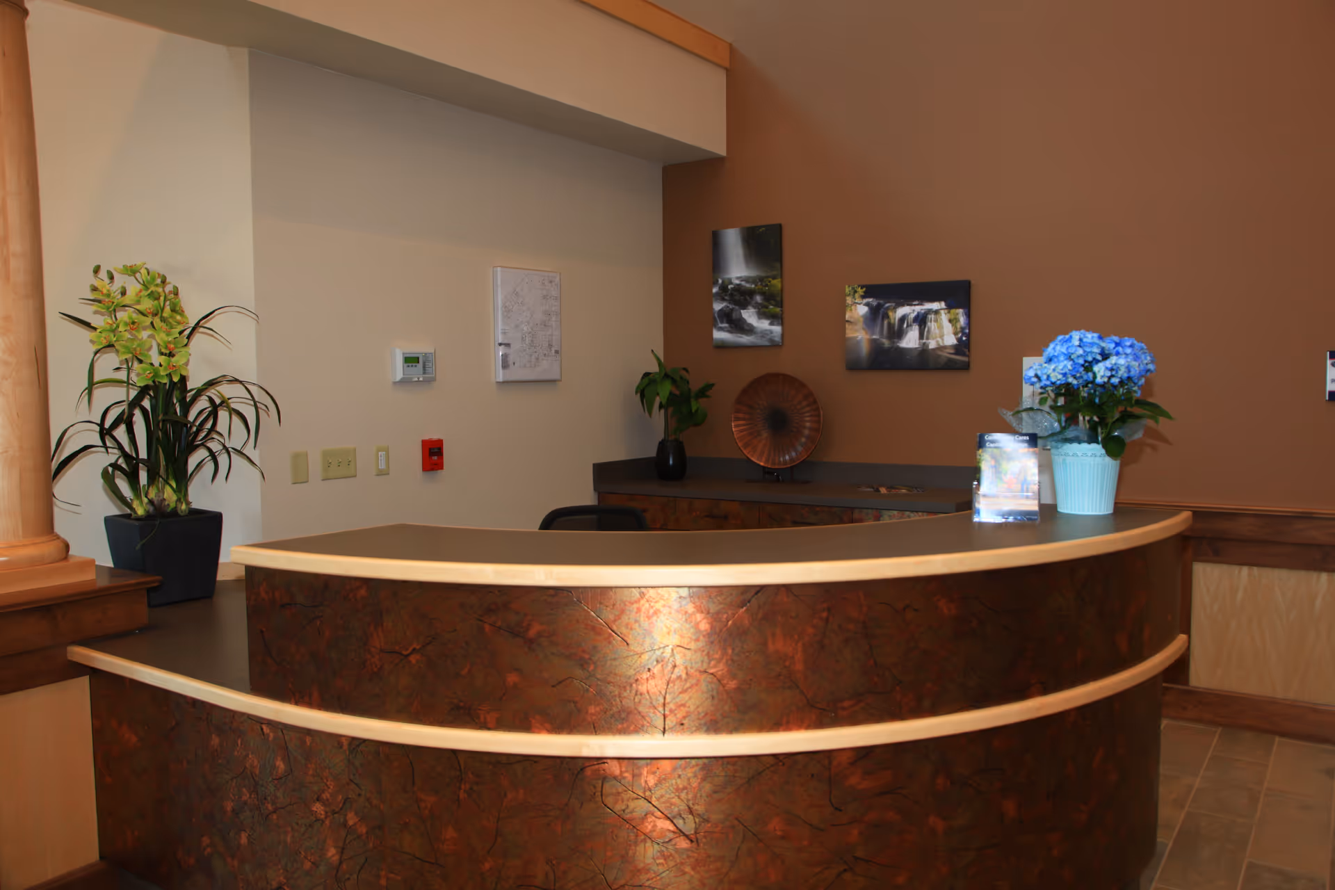 Curved marbled reception desk in a warmly lit lobby with plants and wall art.