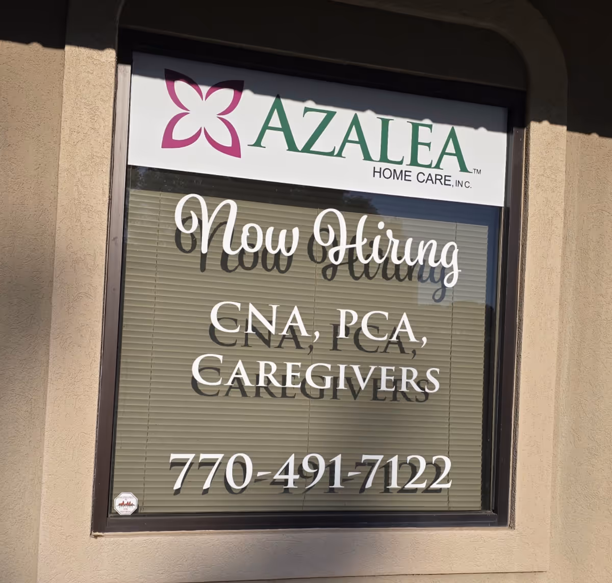 Window sign at Azalea Home Care advertising now hiring CNAs and caregivers.