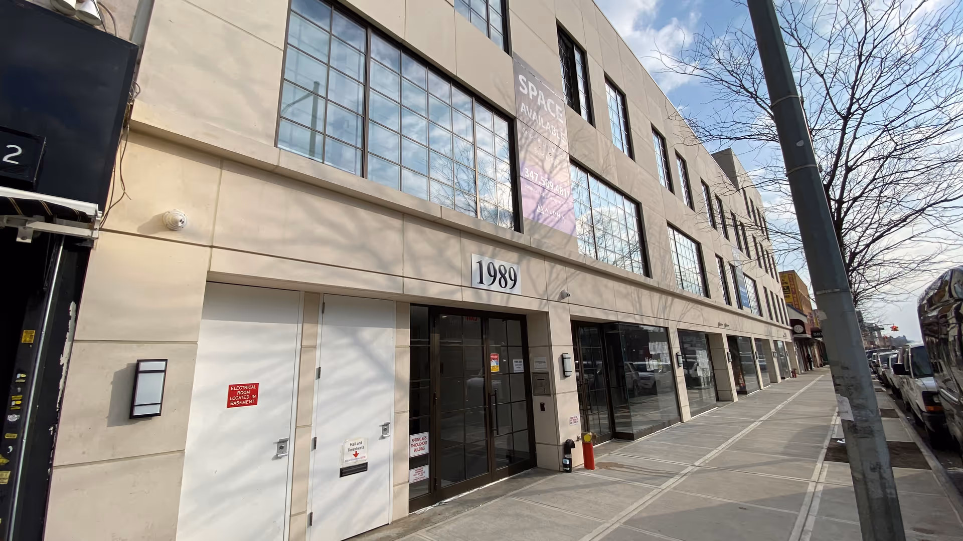 Exterior street-level view of a modern multi-tenant building with large glass storefronts and a numbered entry.