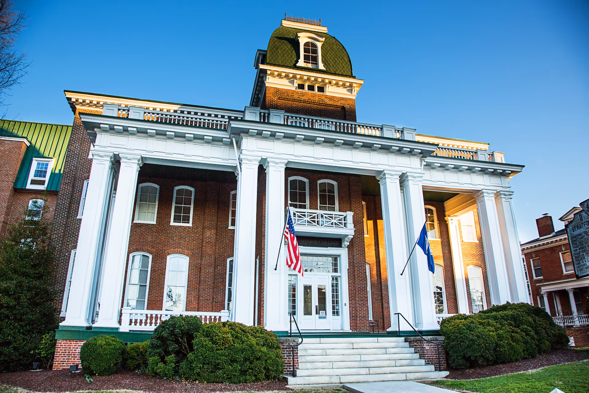 Brick senior living facility with white columns, flags, and a grand front entrance.