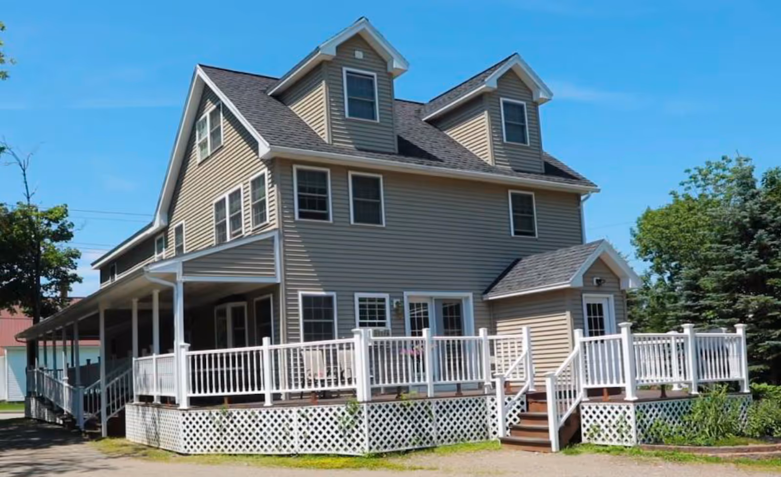 Two-story beige senior living facility with a wraparound porch and white railings.
