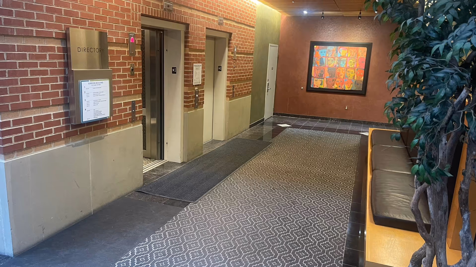 Indoor hallway with brick walls, elevators, directory sign, seating, and artwork.
