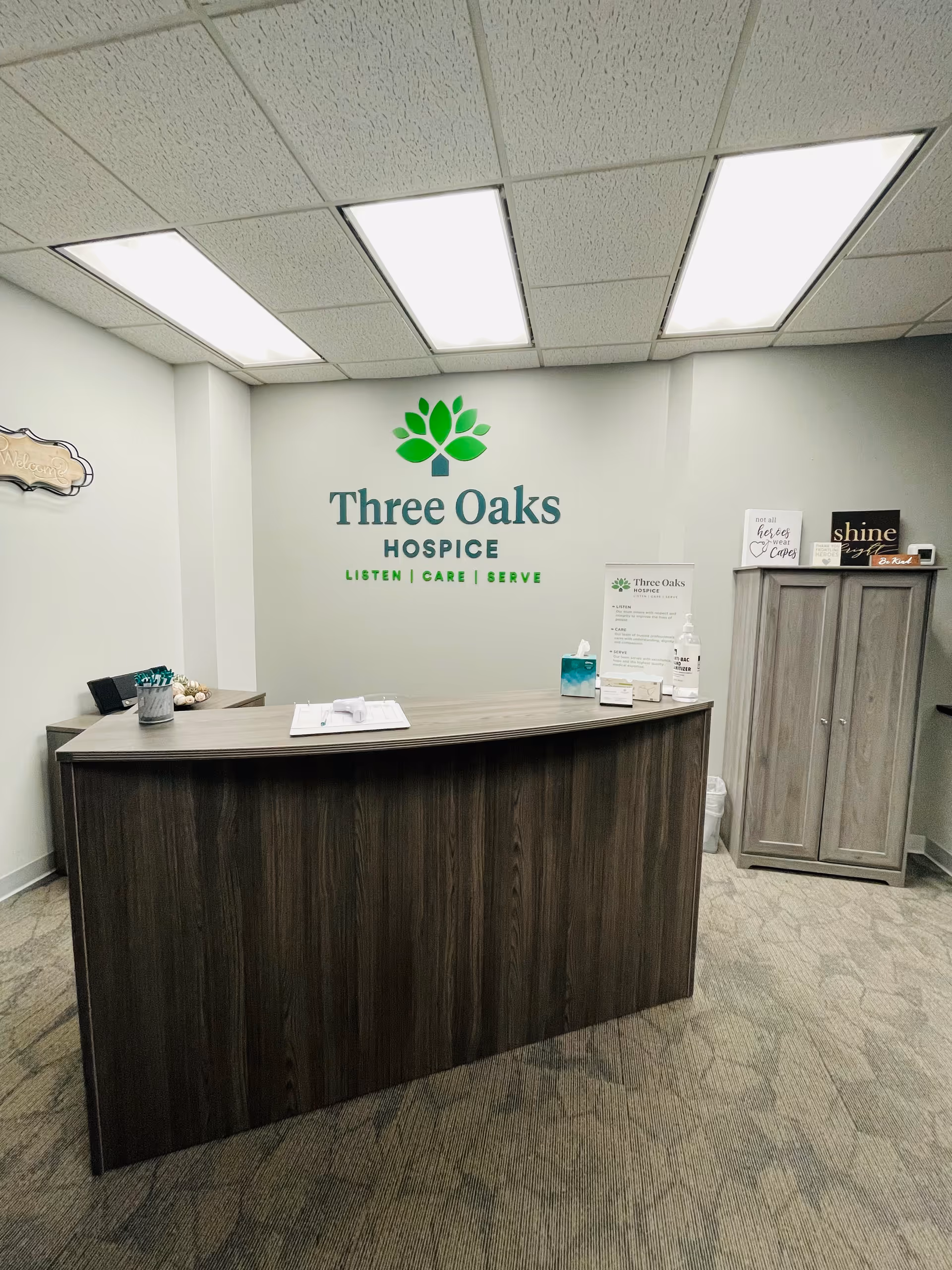 Reception desk in a hospice lobby with a Three Oaks Hospice logo on the wall.