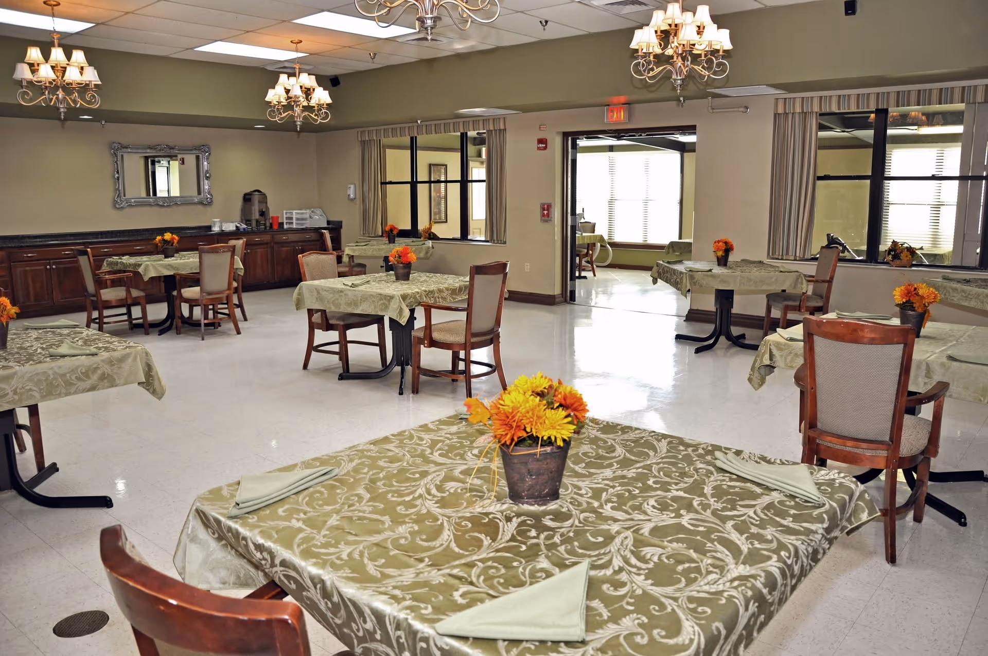 A spacious dining room with patterned tablecloths, chairs, and flower centerpieces.