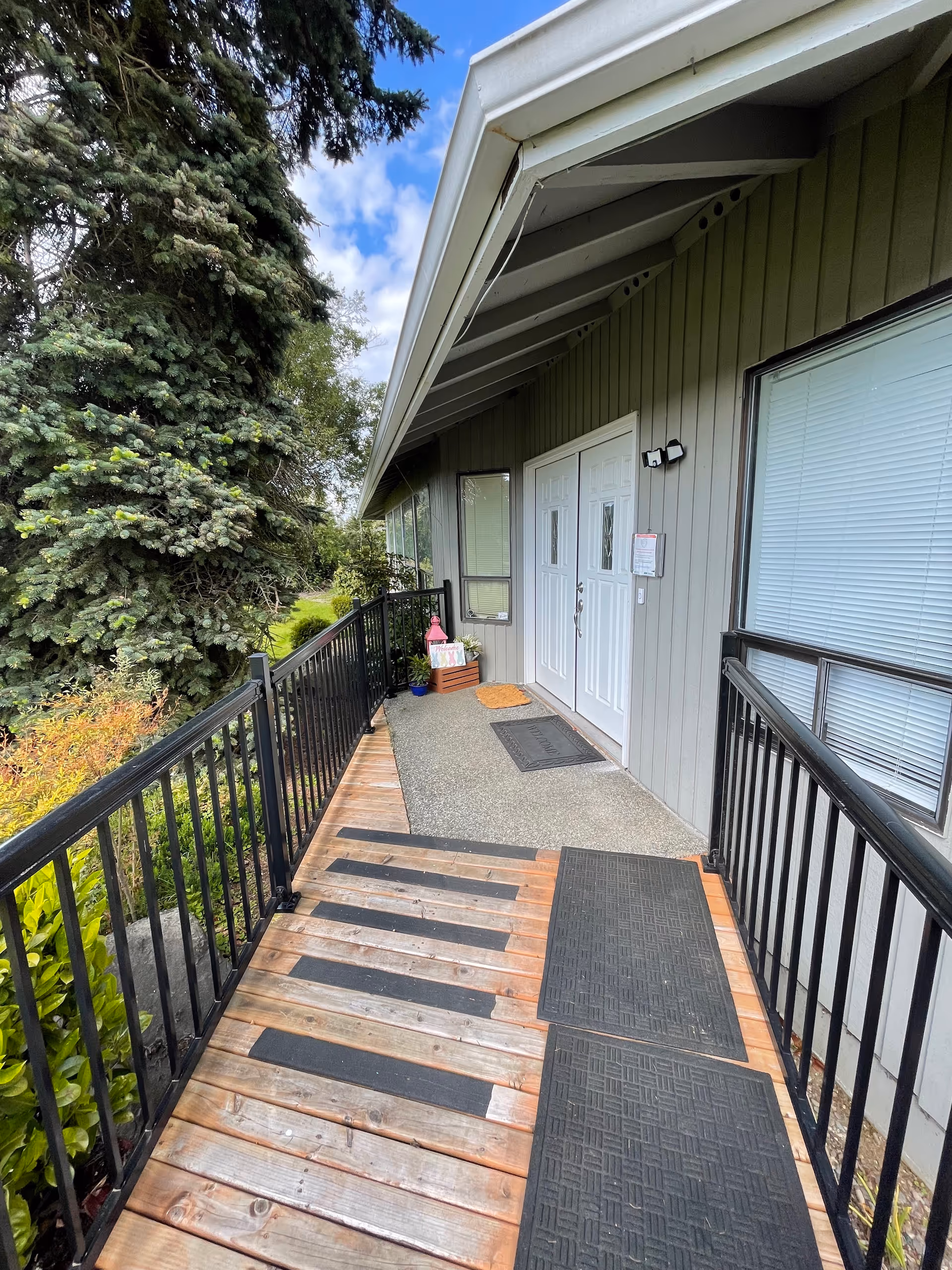Front exterior entrance of Hillside AFH with a wooden ramp, railing, and greenery.