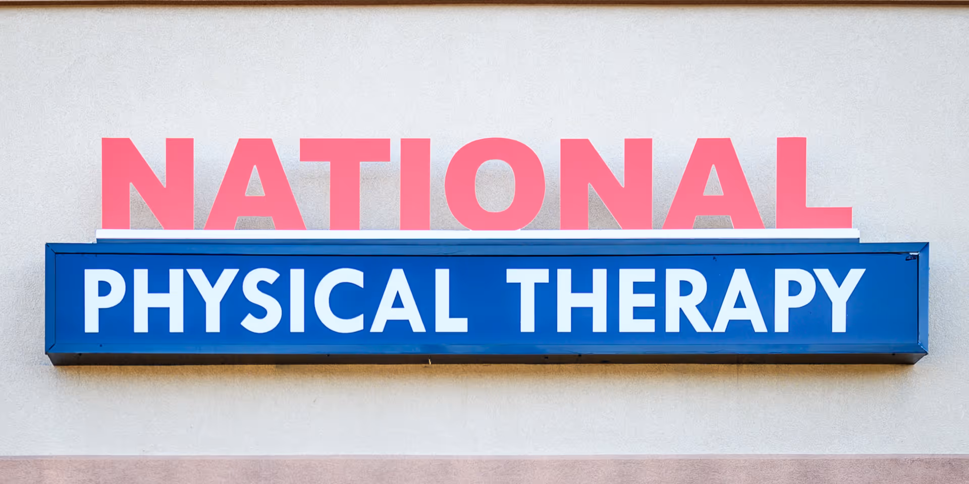 Exterior wall with a blue physical therapy sign and pink NATIONAL above.