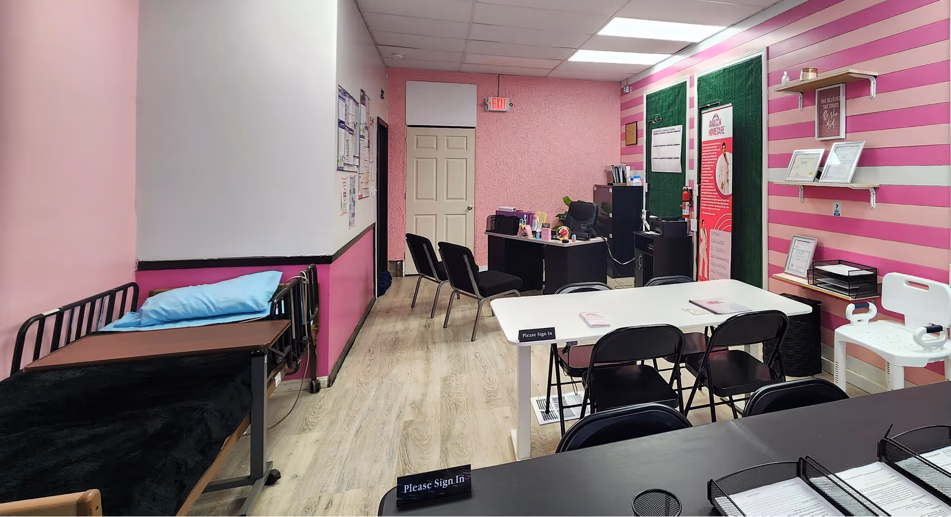 A pink-striped interior room with a desk, chairs, and a medical bed.