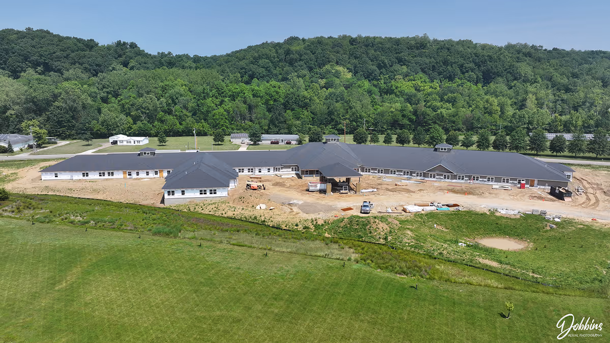 Aerial view of a long, low building under construction in a green rural landscape.