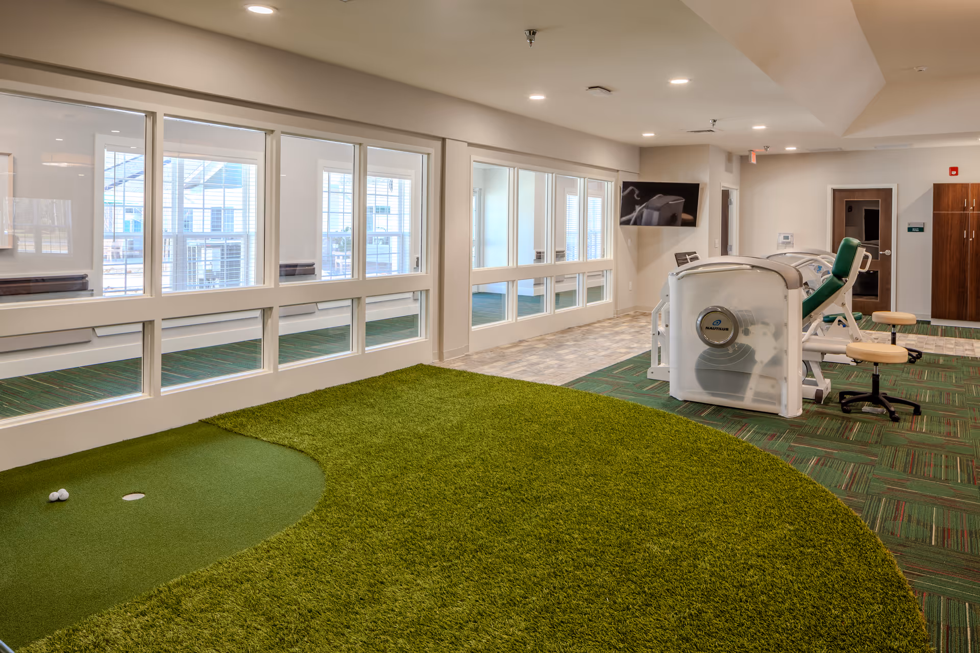 An interior rehab gym featuring a turf putting green and various exercise machines.