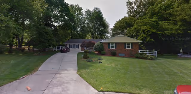 A single-story brick and siding residential building with a driveway leading up to it, surrounded by a well-maintained lawn and trees in the background.