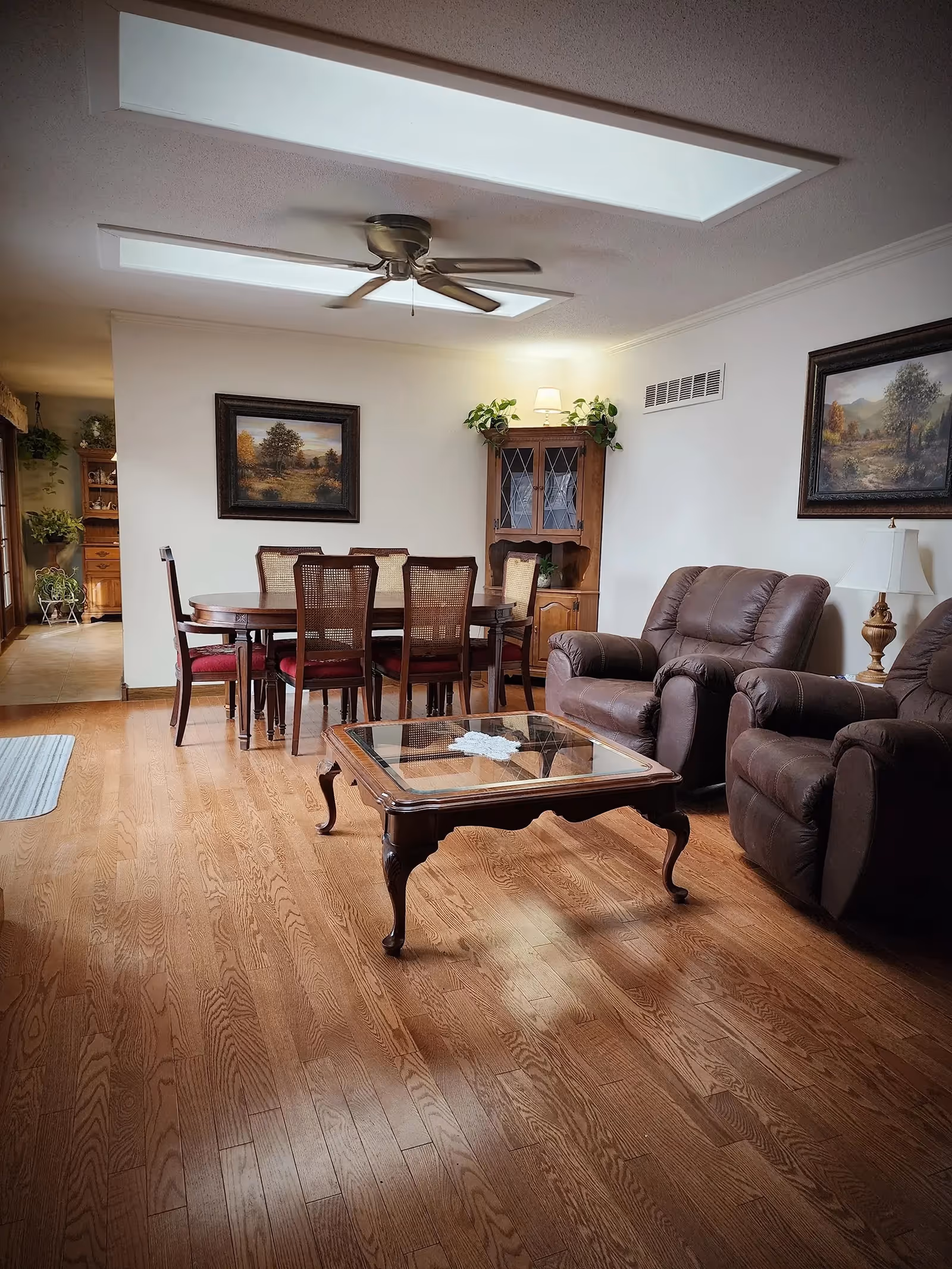 Spacious living room with brown leather recliners, glass coffee table, dining table, and skylights.