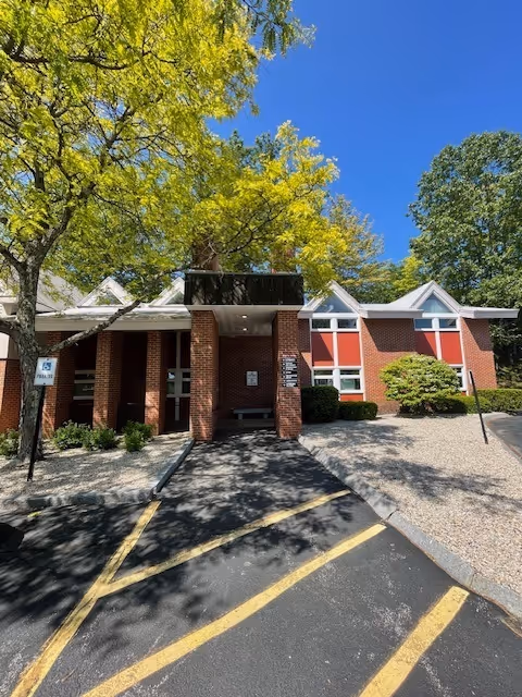 Front view of a brick building entrance with columns and surrounding trees.